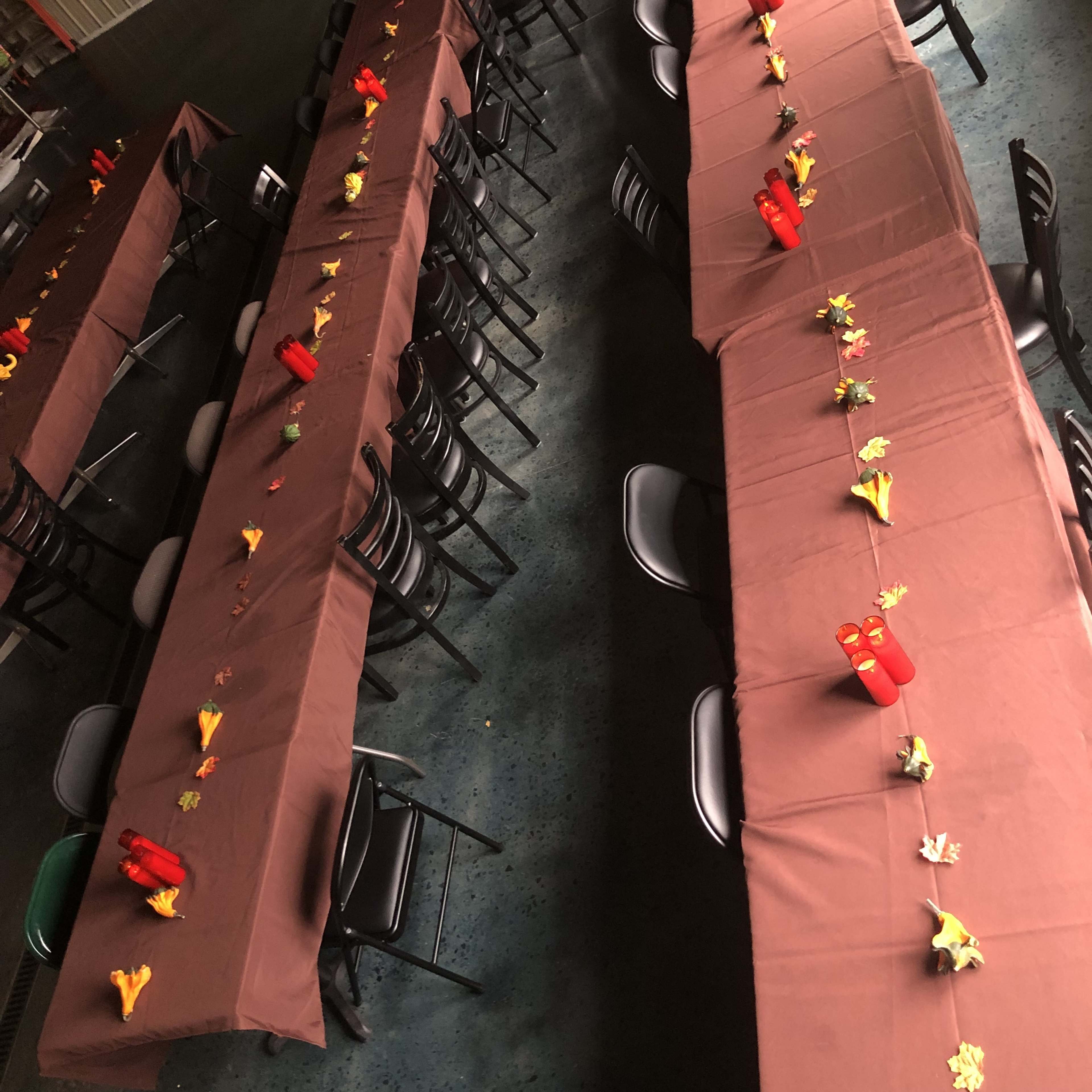 The image shows several long tables covered with brown tablecloths, each decorated with small colorful leaves and candles.