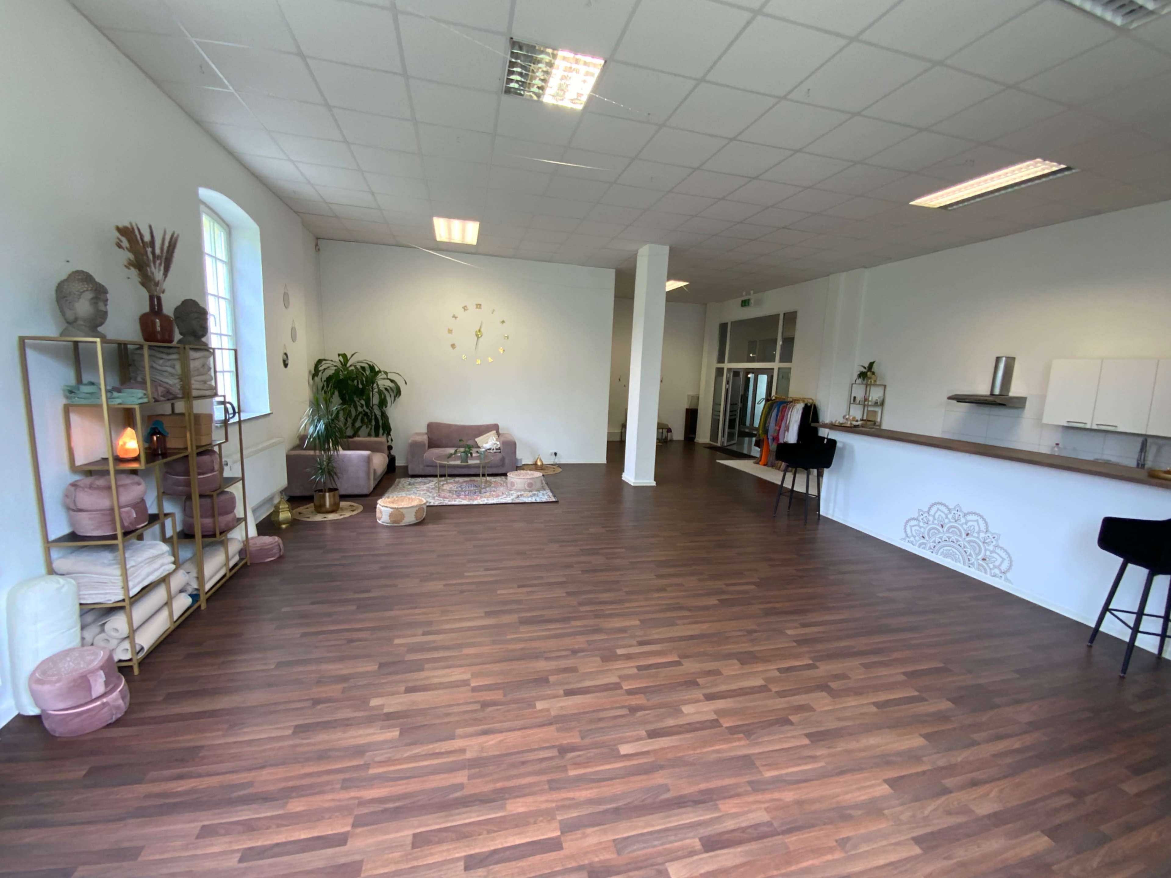 The image shows a spacious, modern room with wooden flooring, a seating area, and various decorative elements.