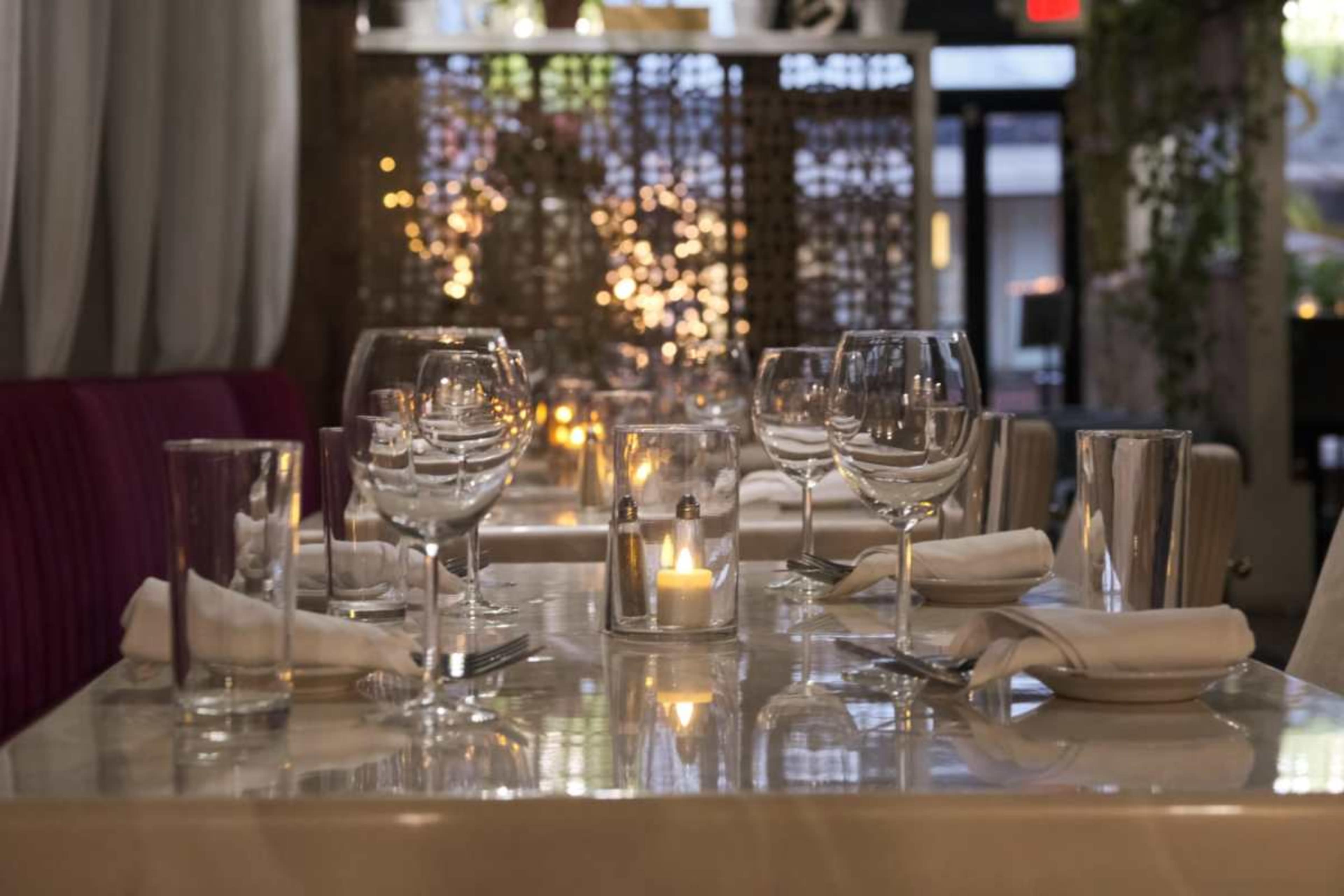 A dining table is set with multiple wine glasses, water glasses, and a lit candle, illuminated by soft lighting in a restaurant.