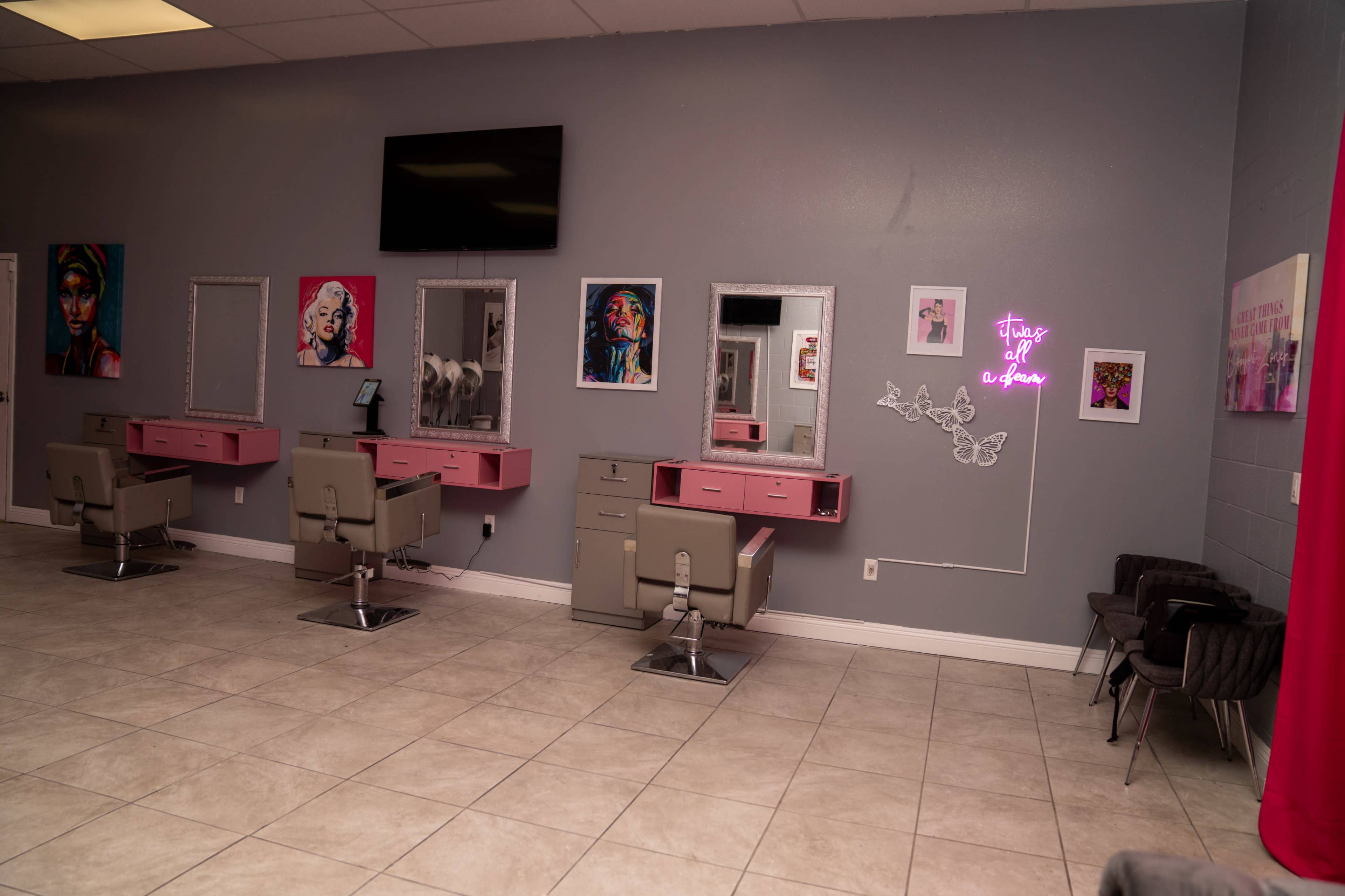 A hair salon interior with pink and gray styling stations, mirrors, artwork on the walls, and a neon sign.