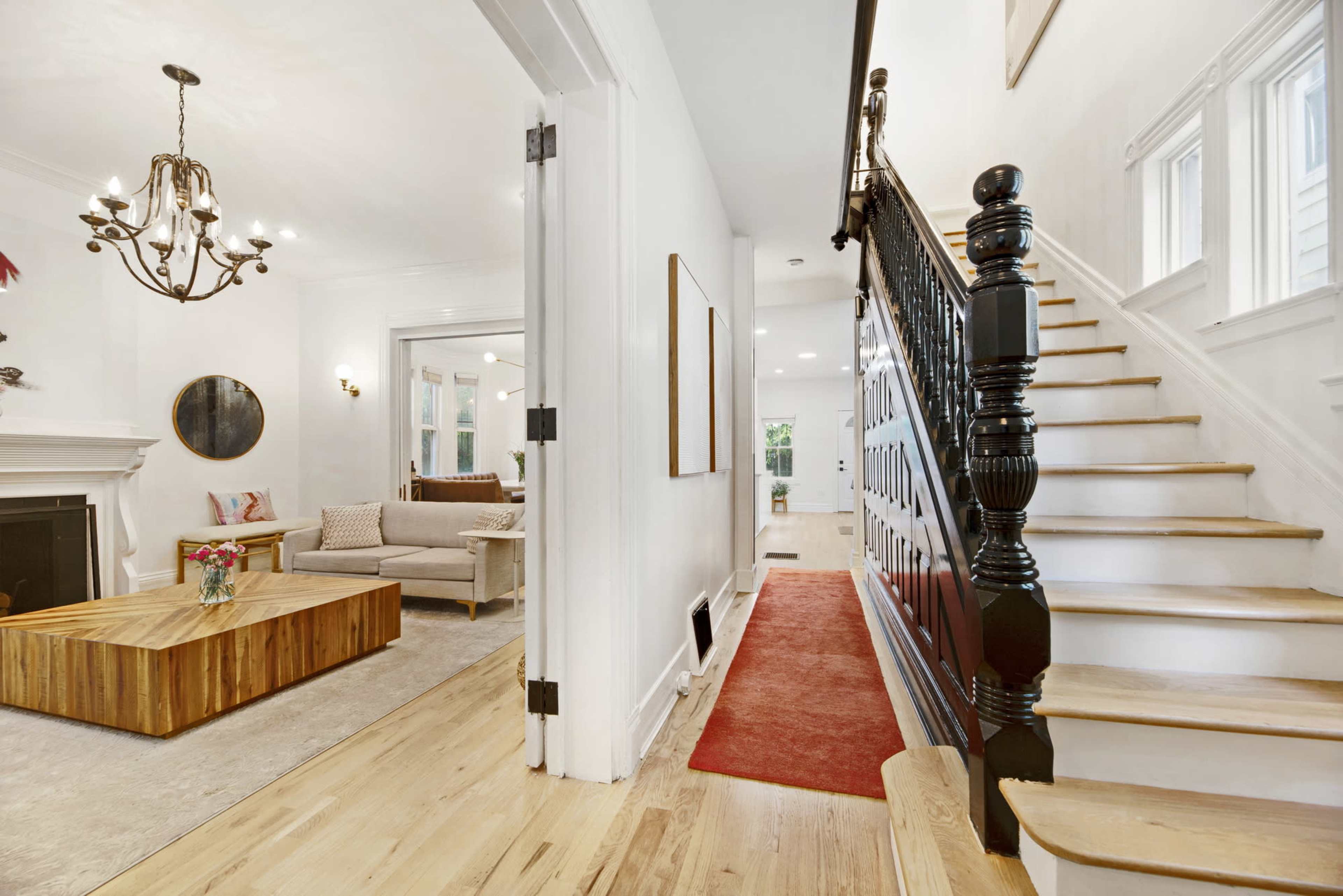 A bright, modern entryway leading to a staircase, with a living room featuring a wooden coffee table and a couch on one side.