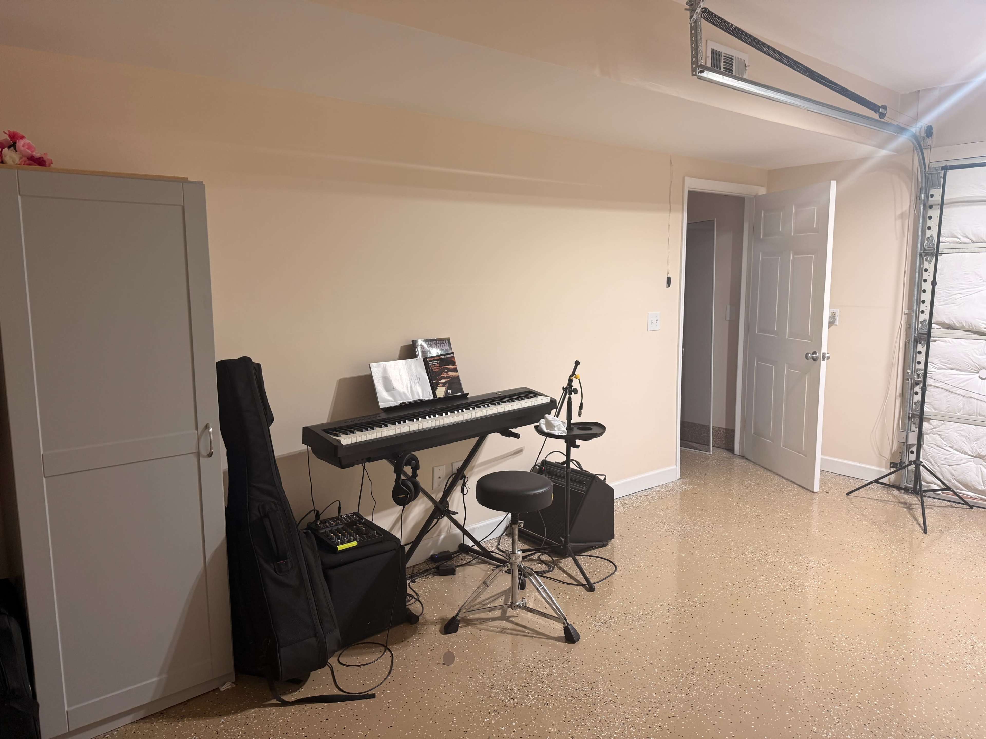 The image shows a garage with a keyboard, microphone, and seating setup, accompanied by a tall cabinet against the wall.