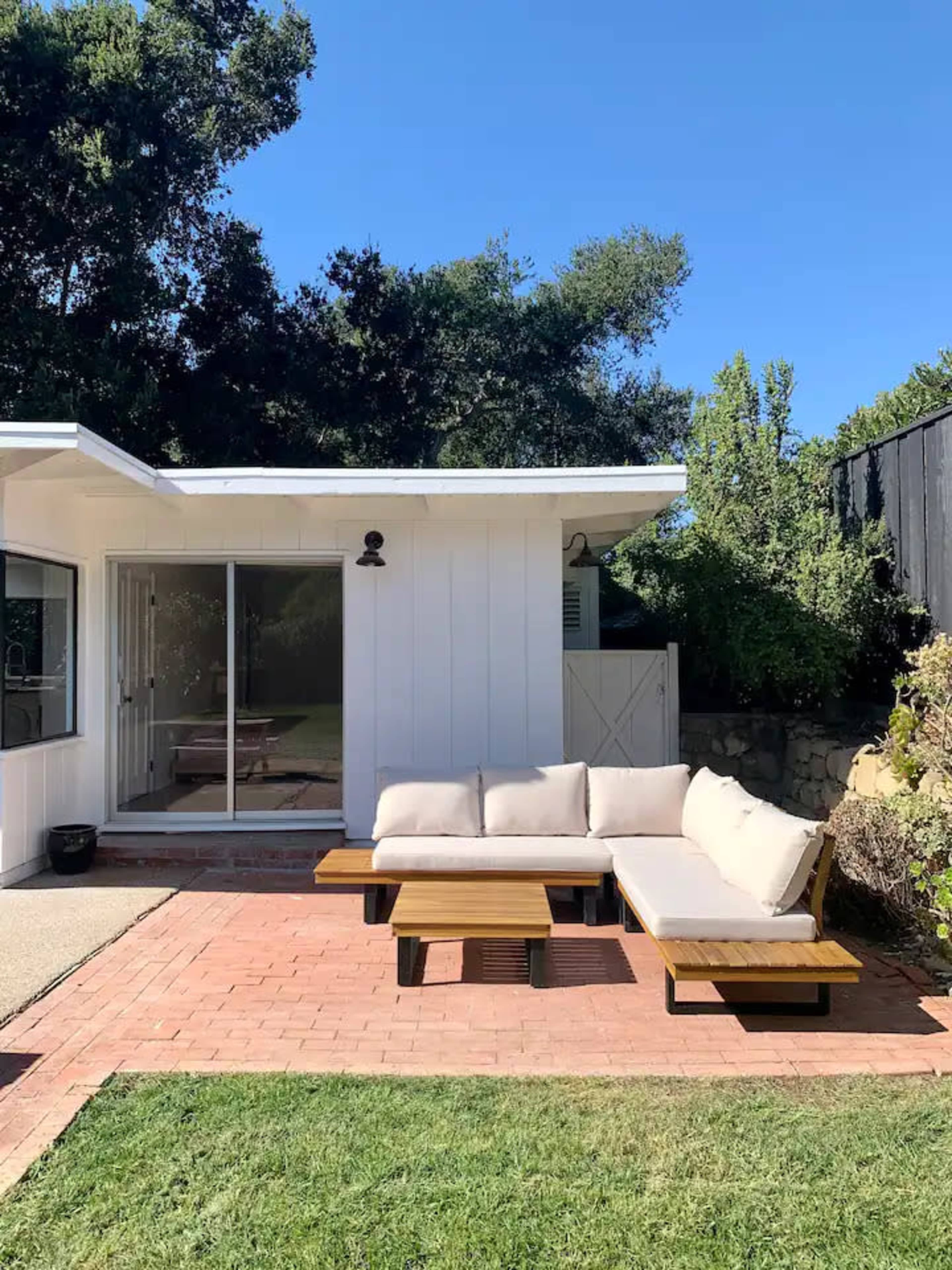 A modern outdoor seating area features a sectional sofa on a brick patio adjacent to a house with a large glass sliding door.