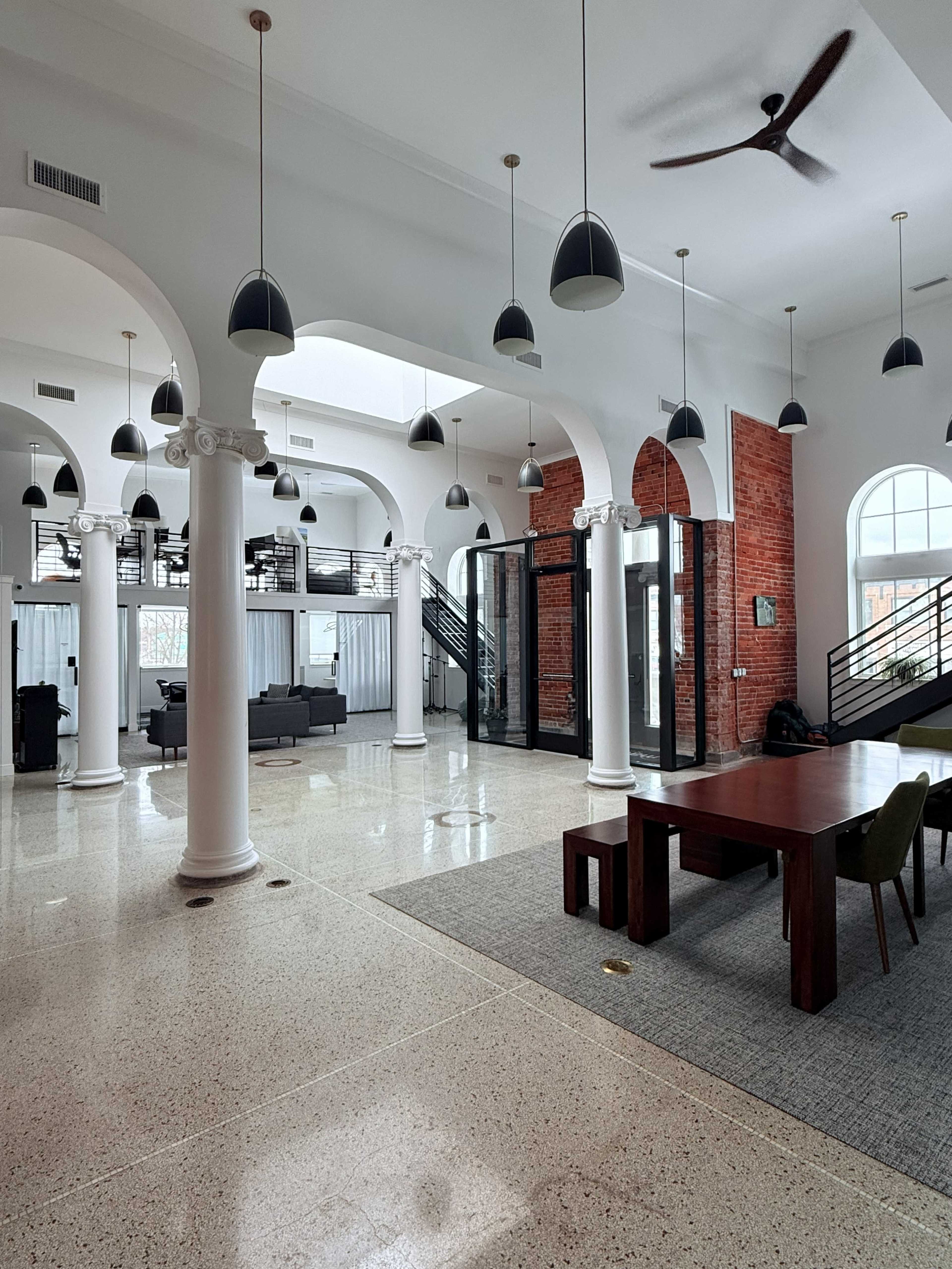 A spacious room features tall white columns, a wooden table, and a mix of modern and industrial design elements.