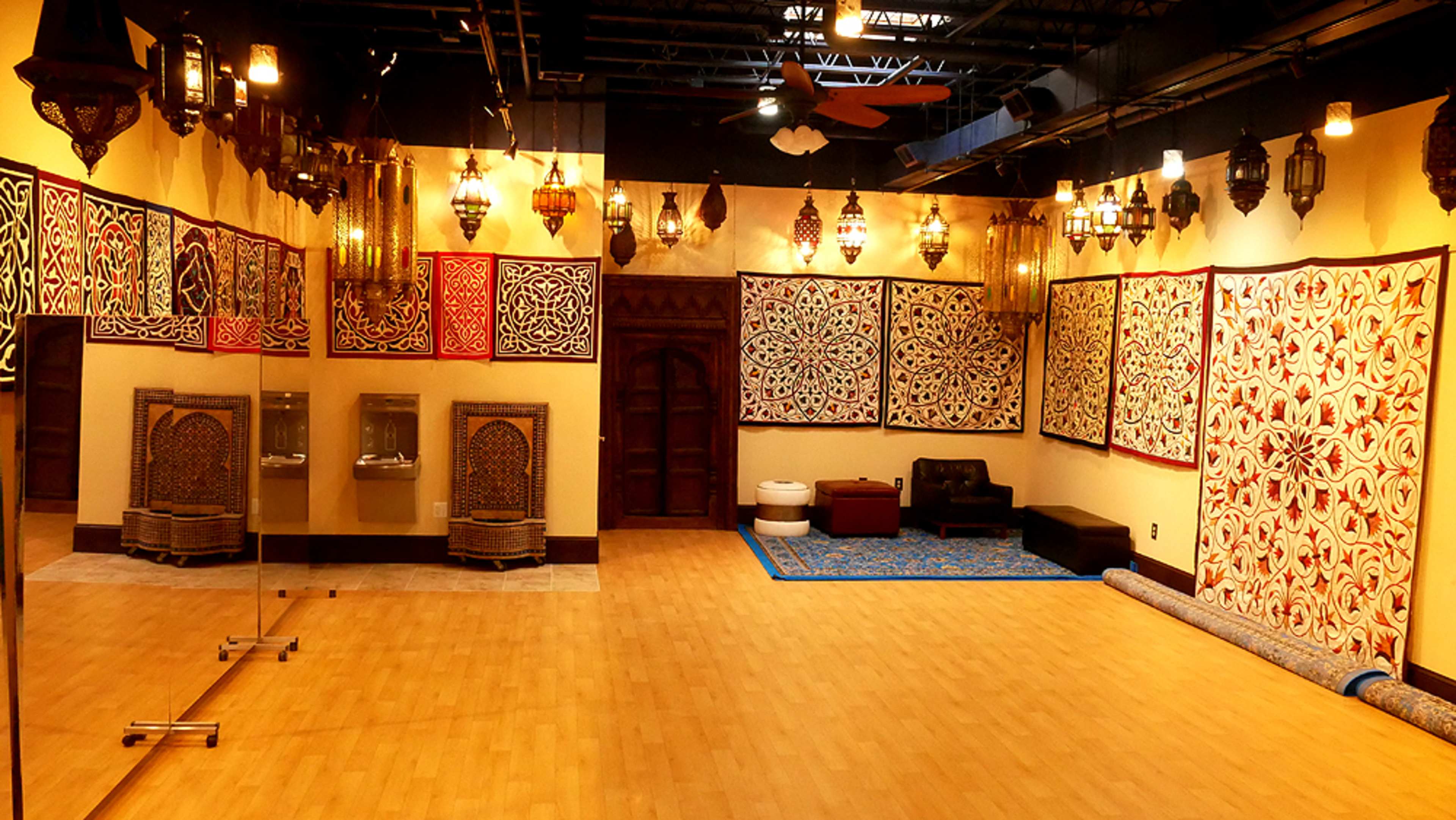A spacious room with decorative wall art, intricate lanterns hanging from the ceiling, and a mix of seating and mirrors against the walls.
