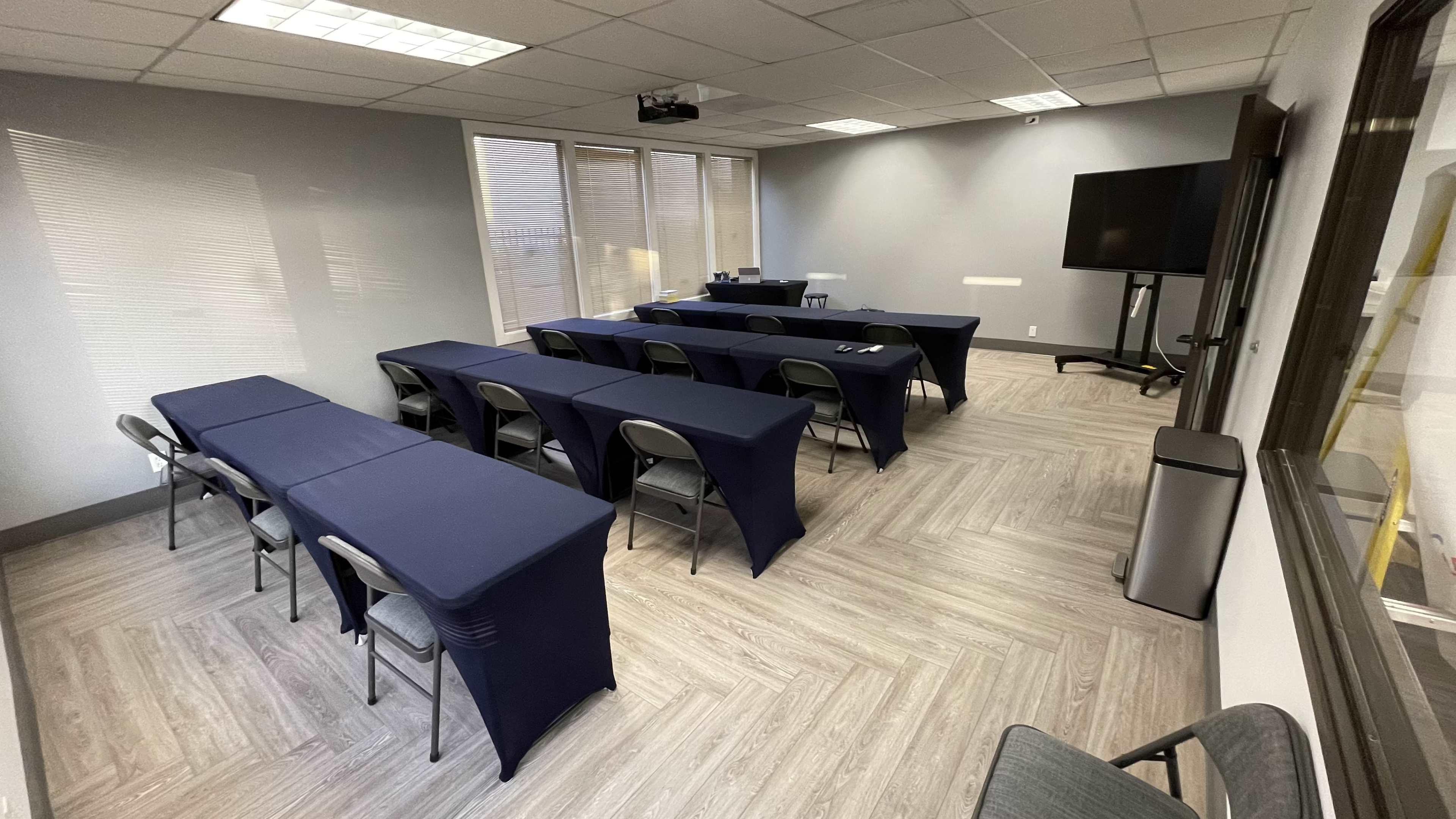 The image shows a conference room with two rows of tables covered in navy blue cloth, facing a screen at the front of the room.