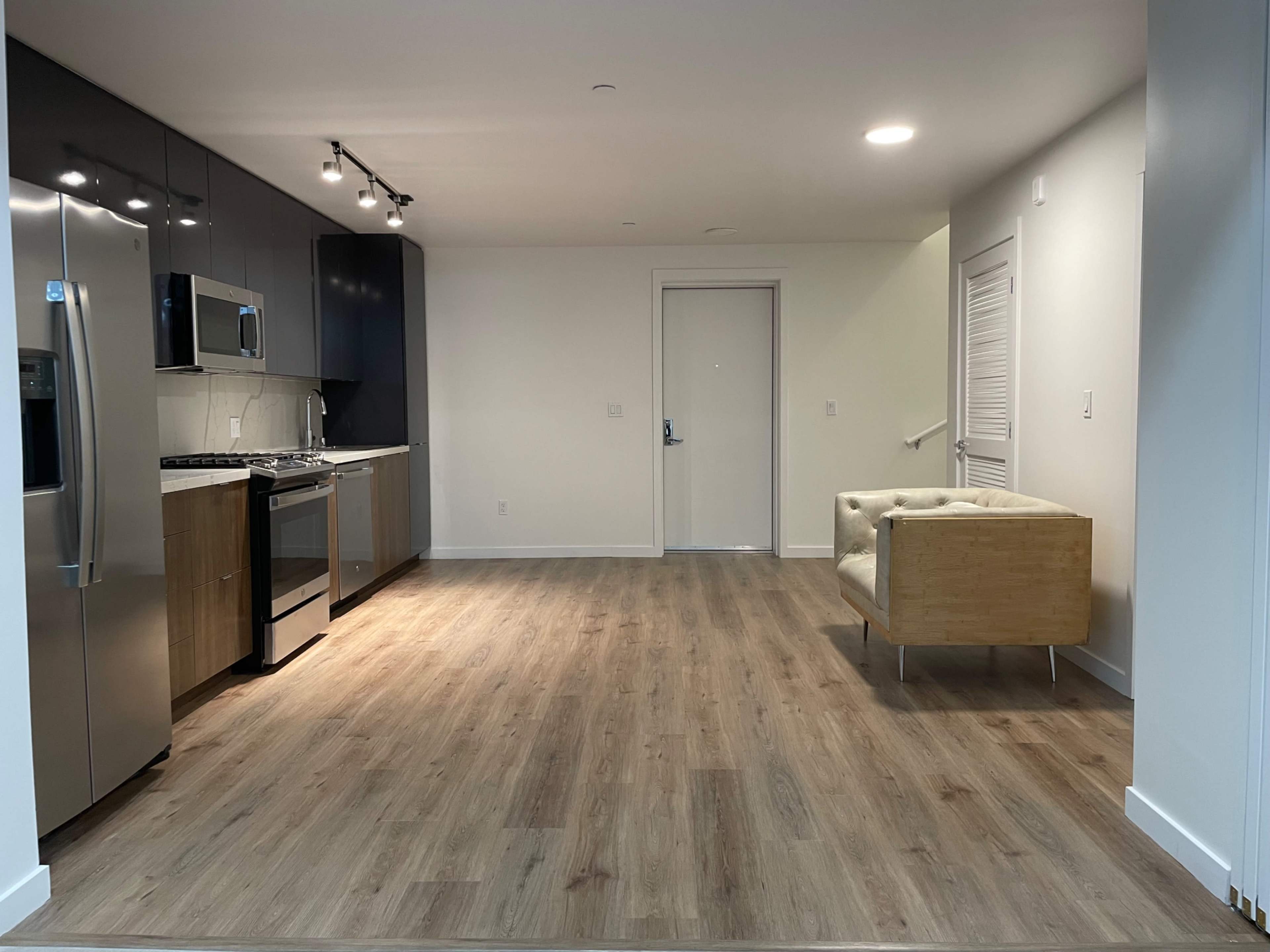 A modern, empty kitchen and living area with light wood flooring and minimal furnishings.