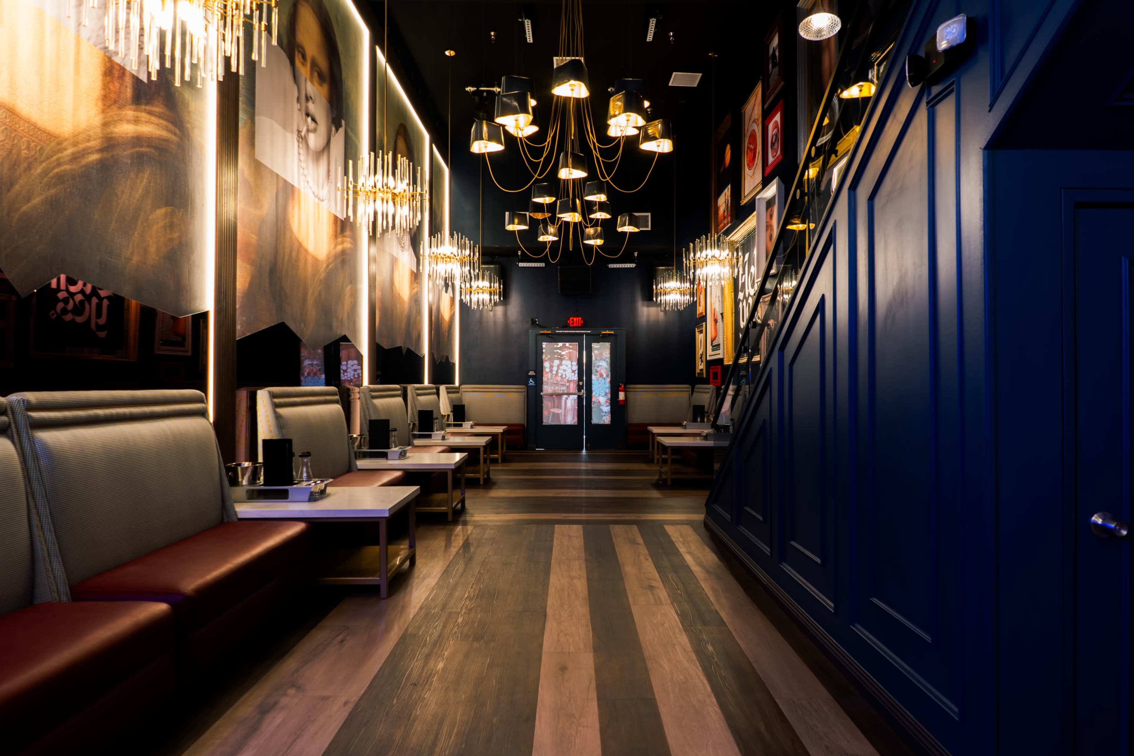 A modern restaurant interior with booths along the walls, a wooden floor, and decorative chandeliers hanging from the ceiling.