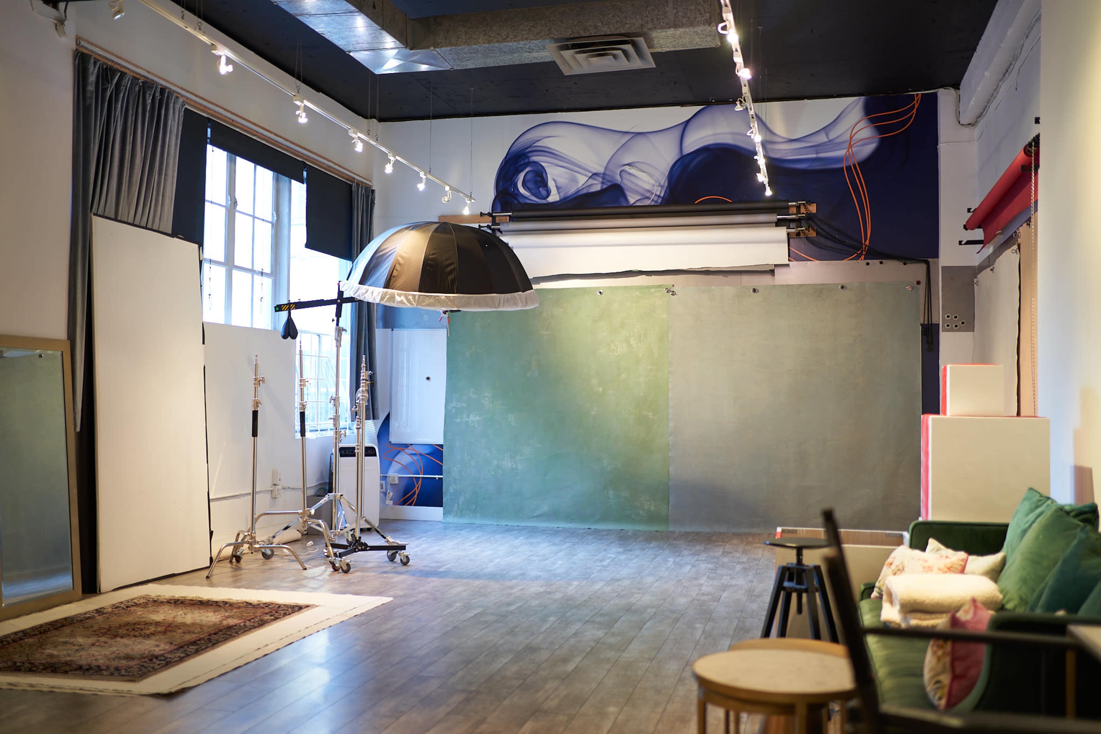 The image shows a photography studio with a green backdrop, various props, and a large light umbrella setup.