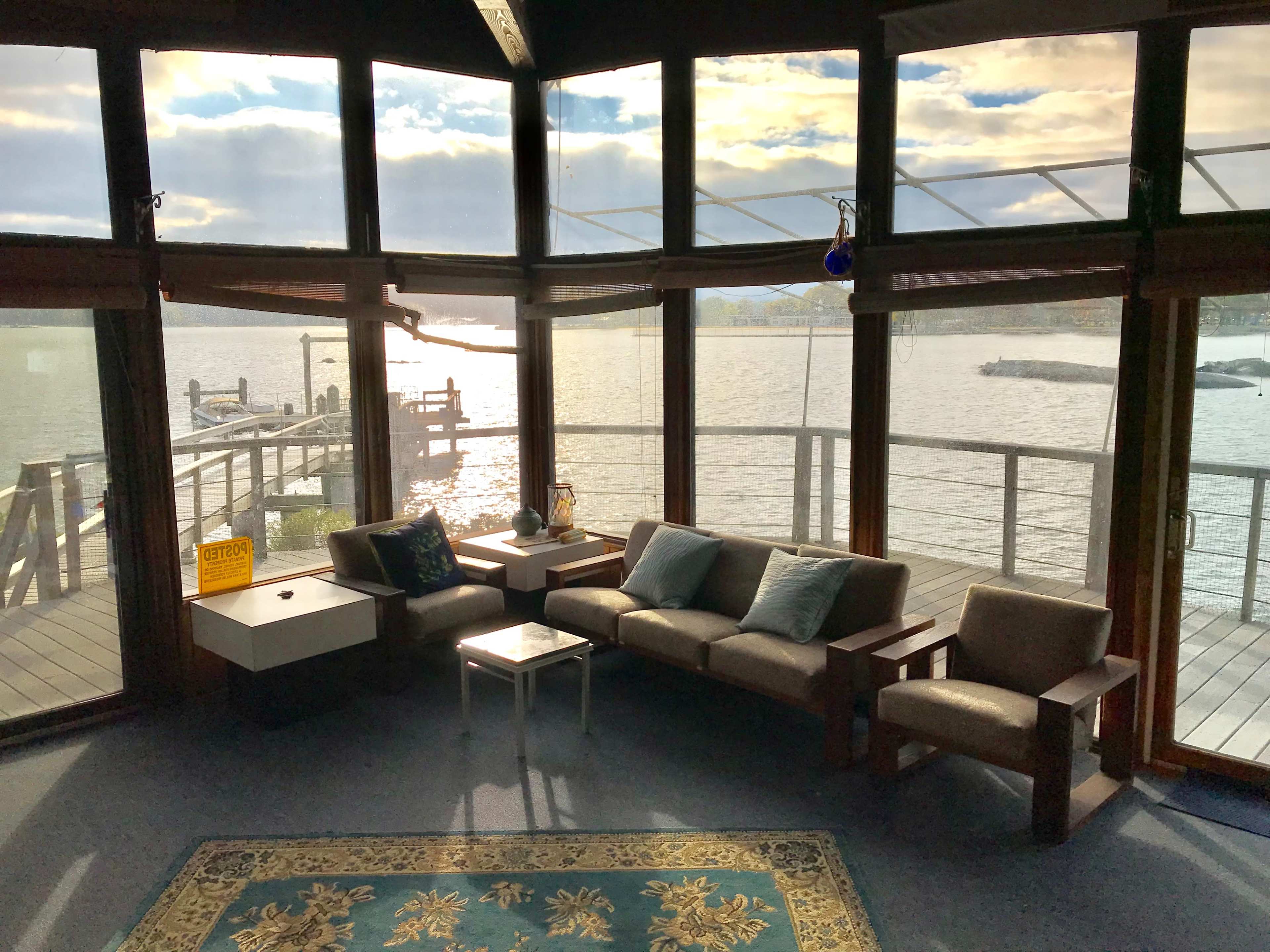A cozy sitting area with a view of a lake features large windows, a small coffee table, and a blue area rug.