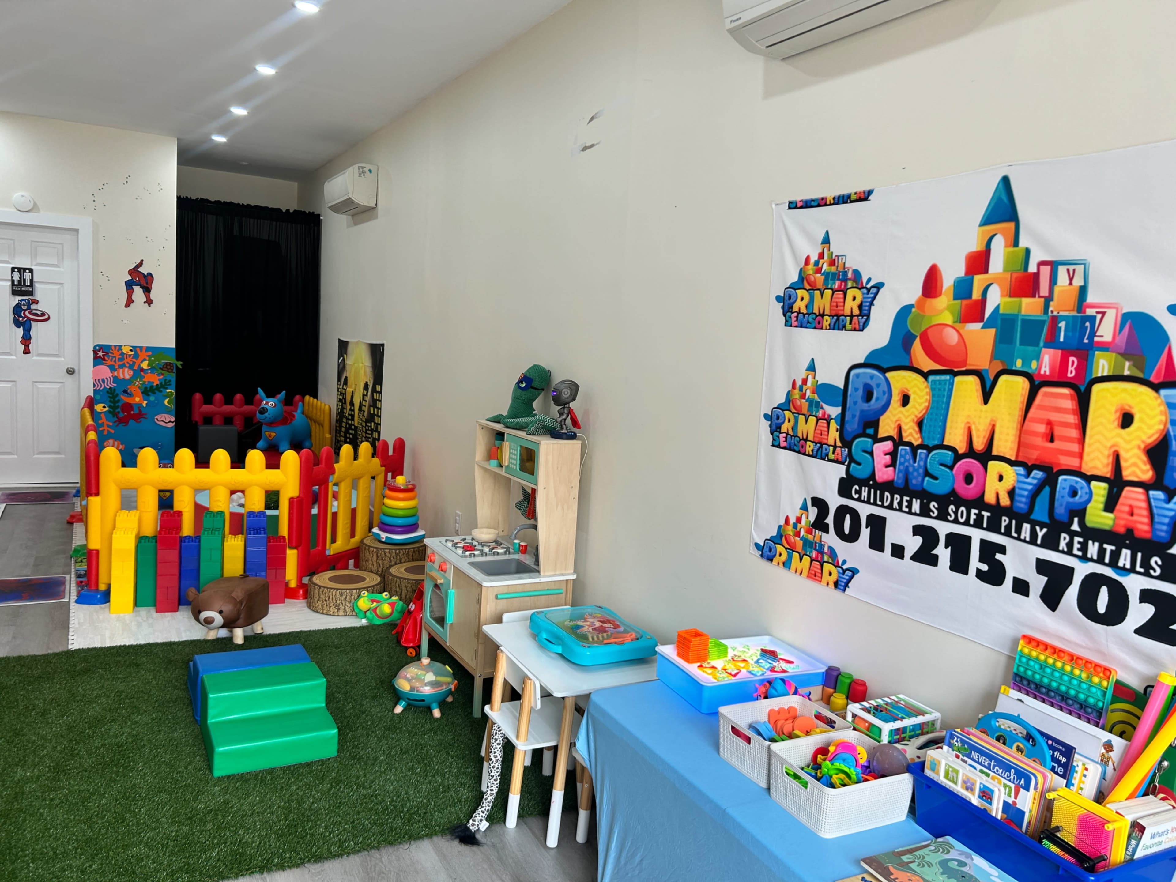 The image shows a colorful indoor play area equipped with soft play structures, toys, and a banner for a children's play rental service.