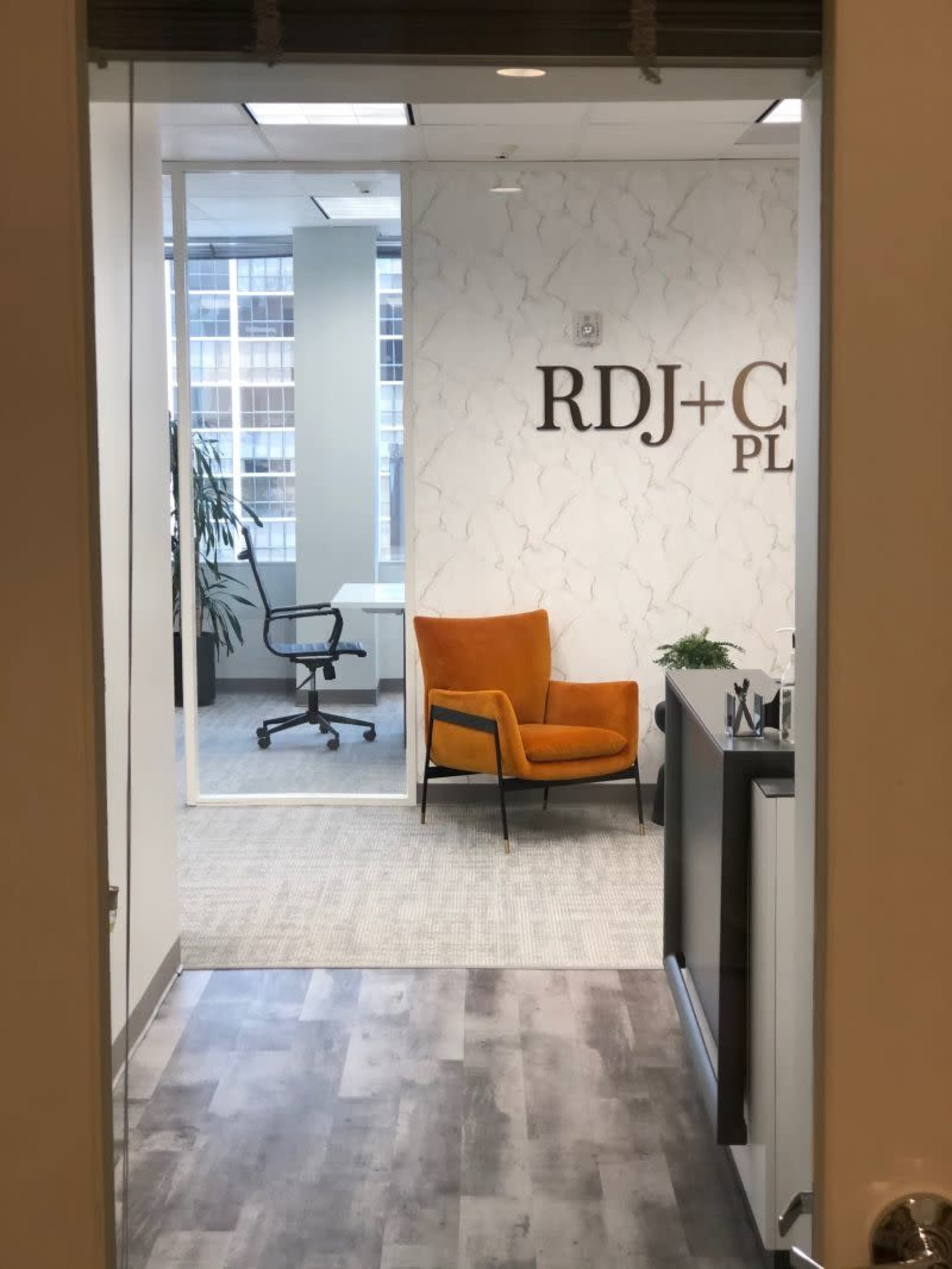 An office interior with a view of an orange chair, a glass-walled conference room, and a reception area.