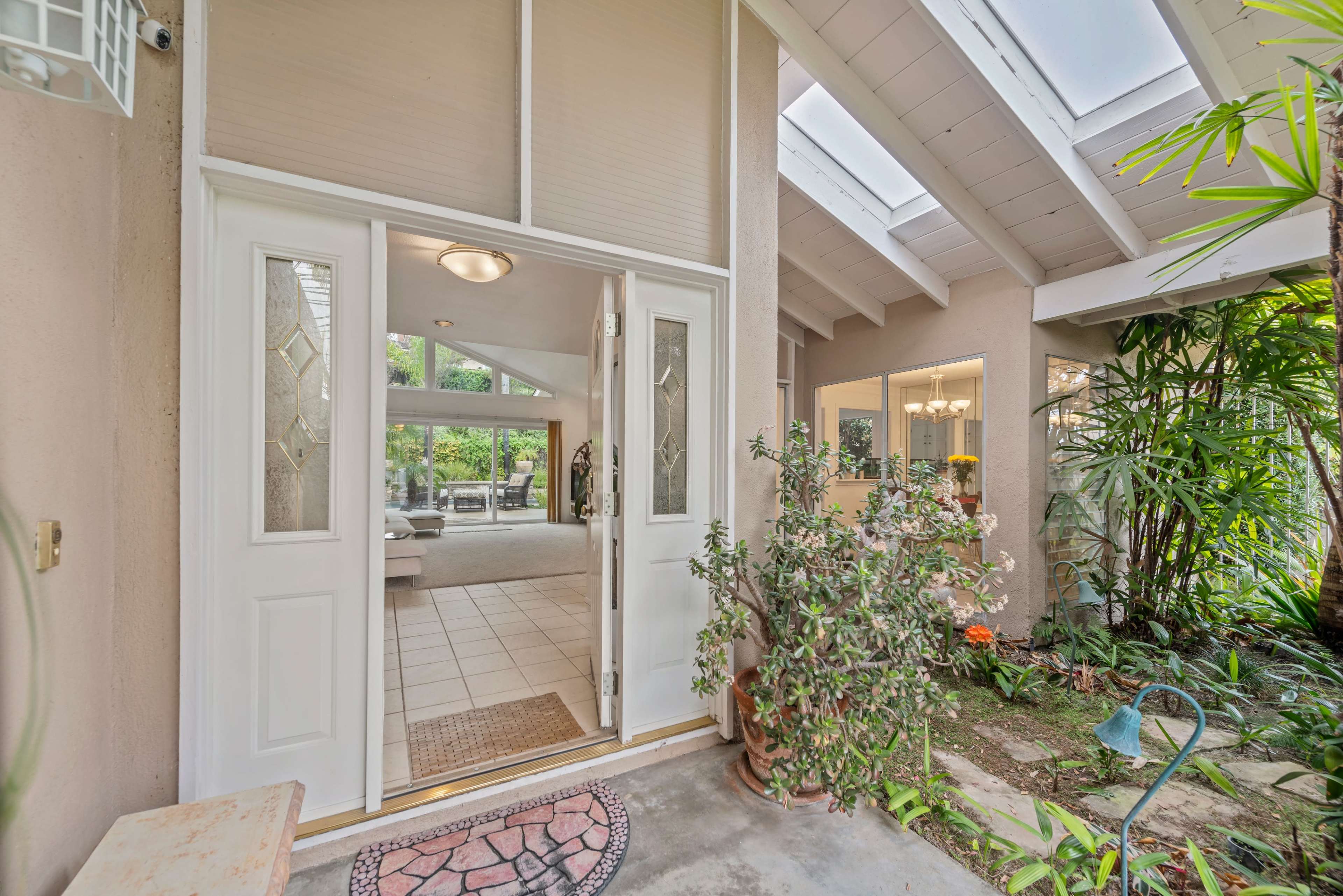 The entrance features double doors opening into a brightly lit foyer surrounded by plants and natural light.