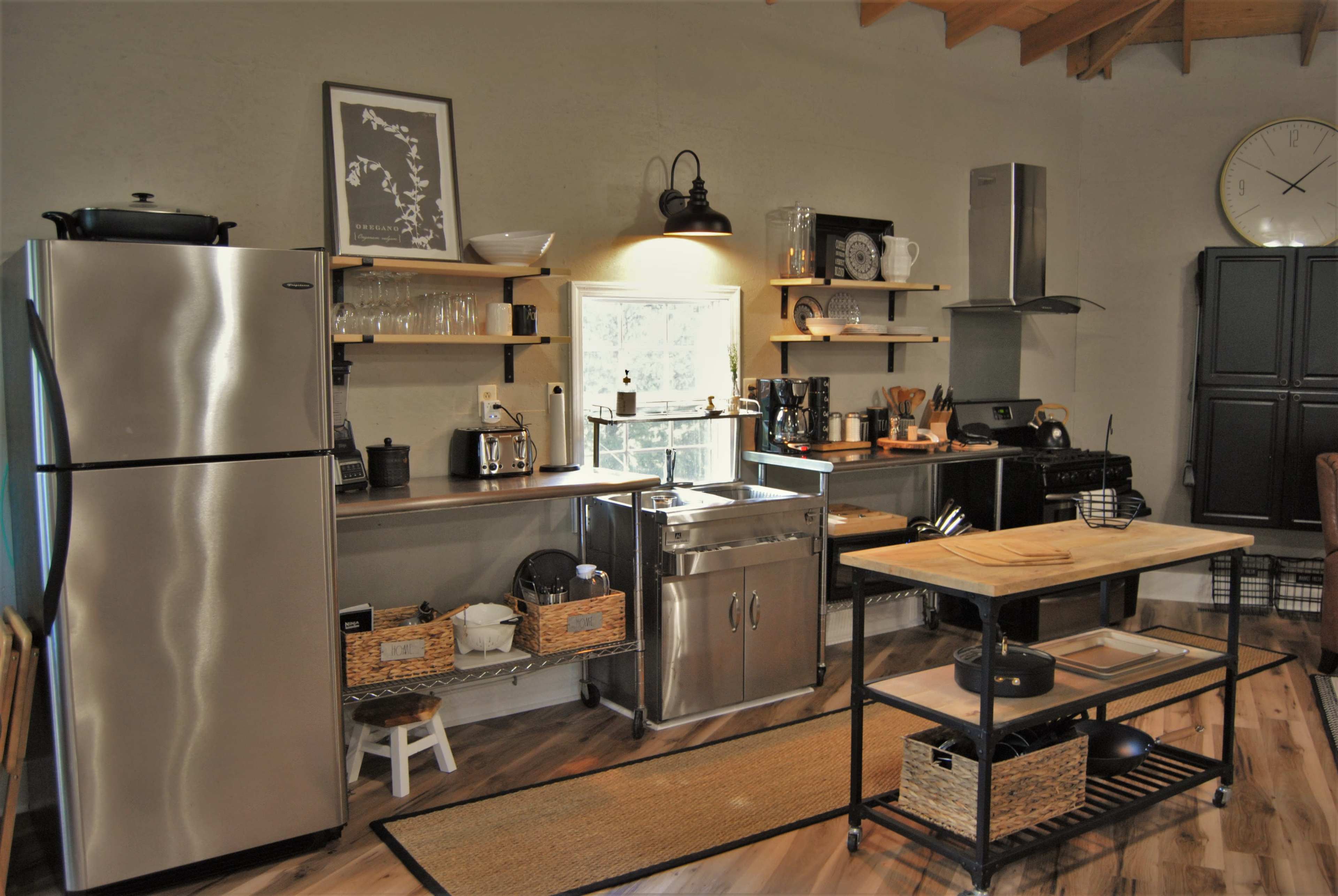 A modern kitchen featuring stainless steel appliances, wooden shelves with kitchenware, and a central island with a metal frame.