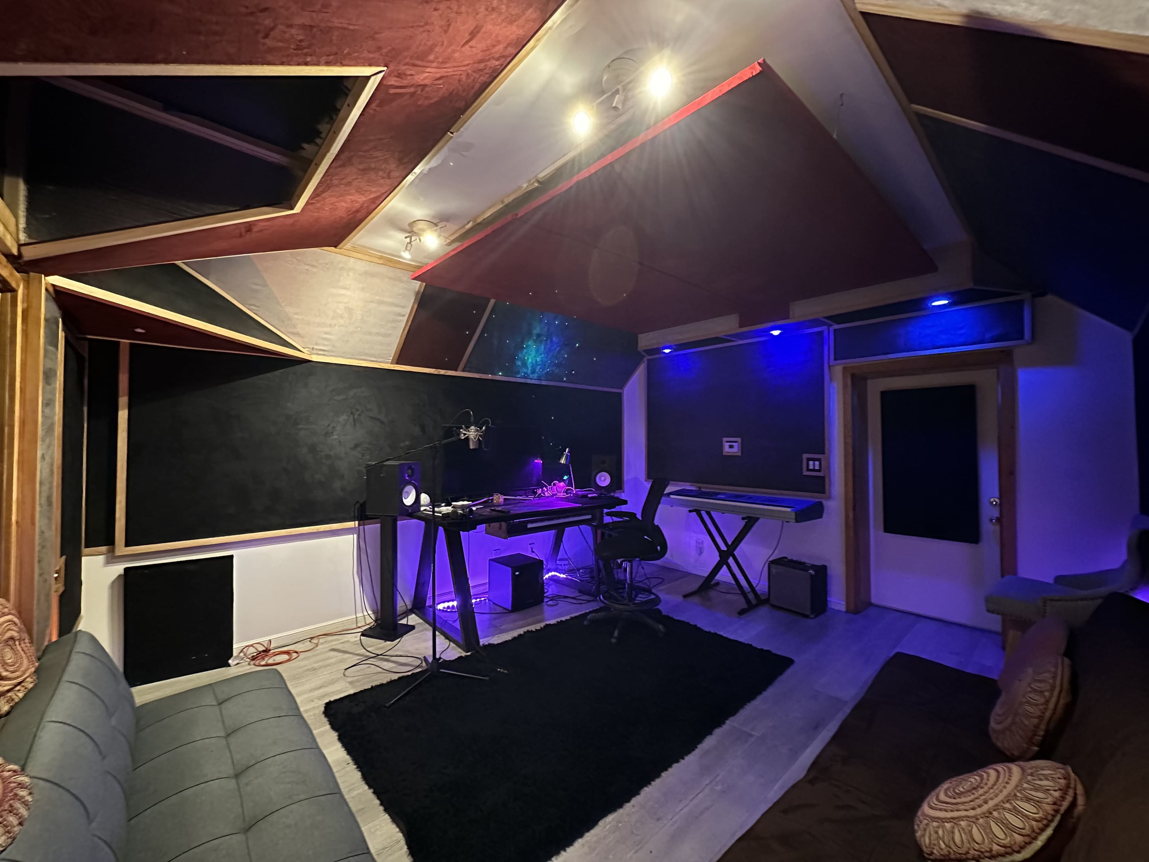 A music studio with acoustic panels, a keyboard, and a mixing desk set up under ambient lighting.