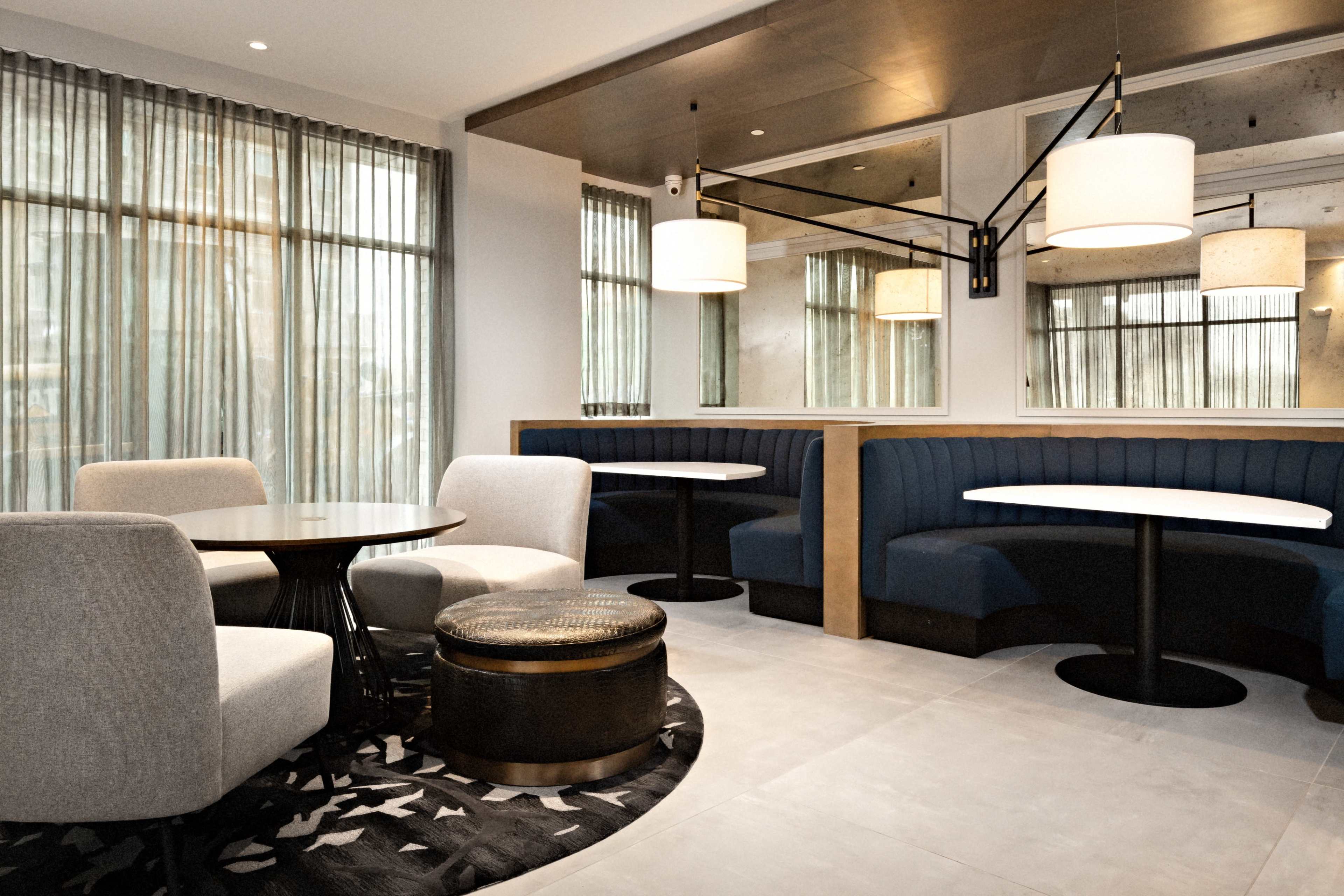 A modern café interior features soft seating, circular tables, and large windows with sheer curtains.