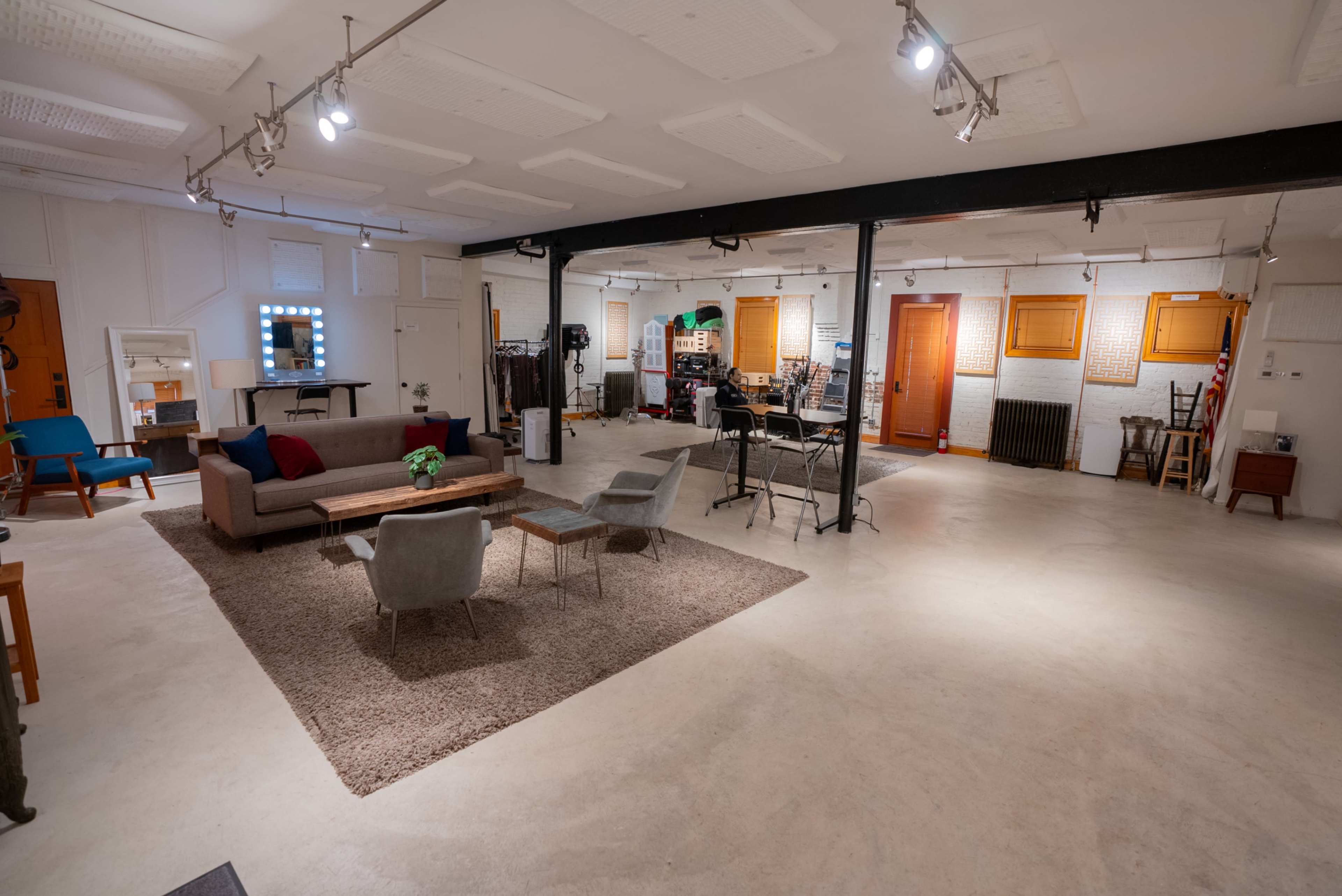 A spacious, well-lit studio with a large rug, seating areas, and various furniture pieces against white walls.