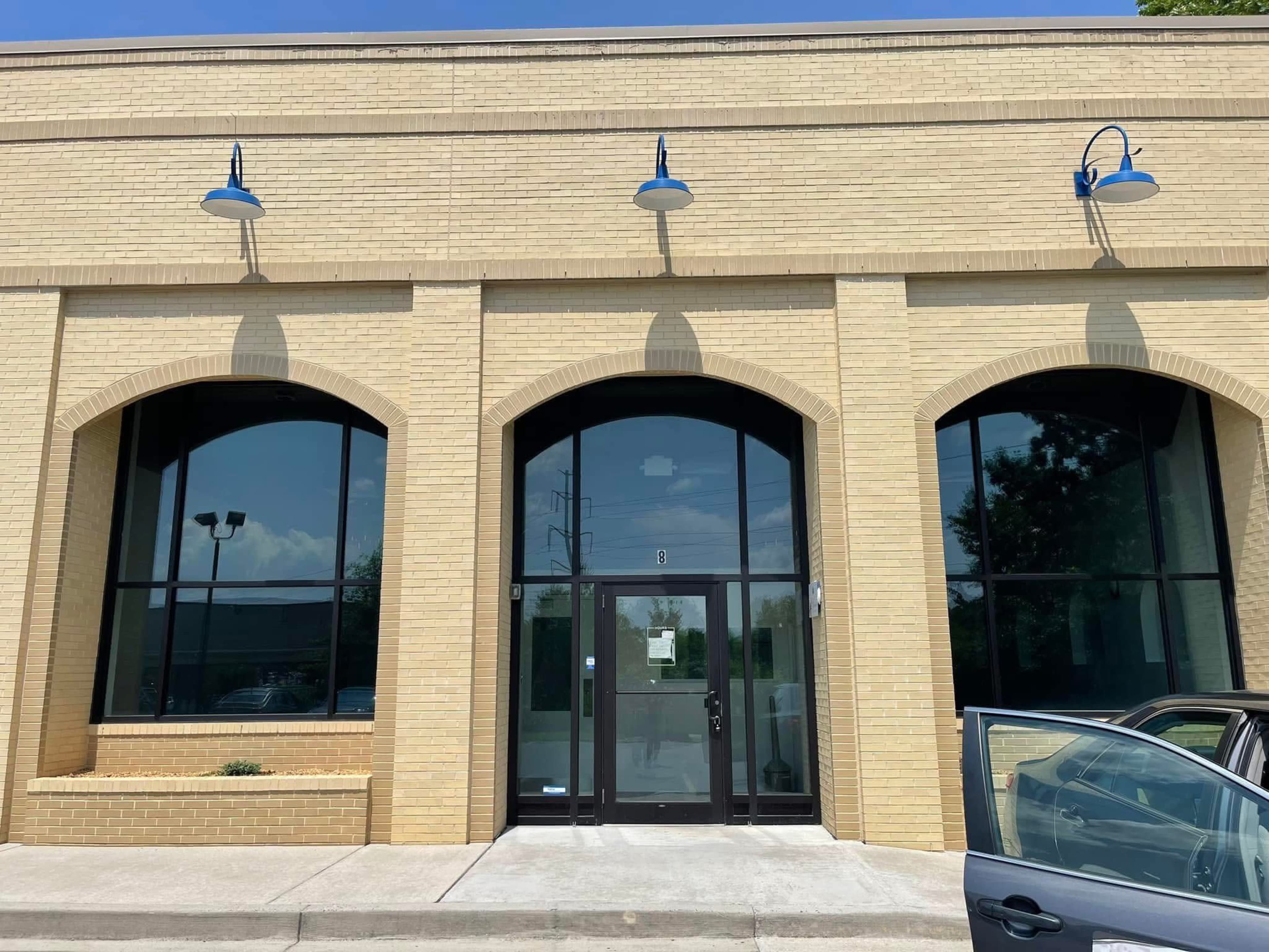 The image shows a brick building facade with three large arched windows and two blue wall-mounted lights above.