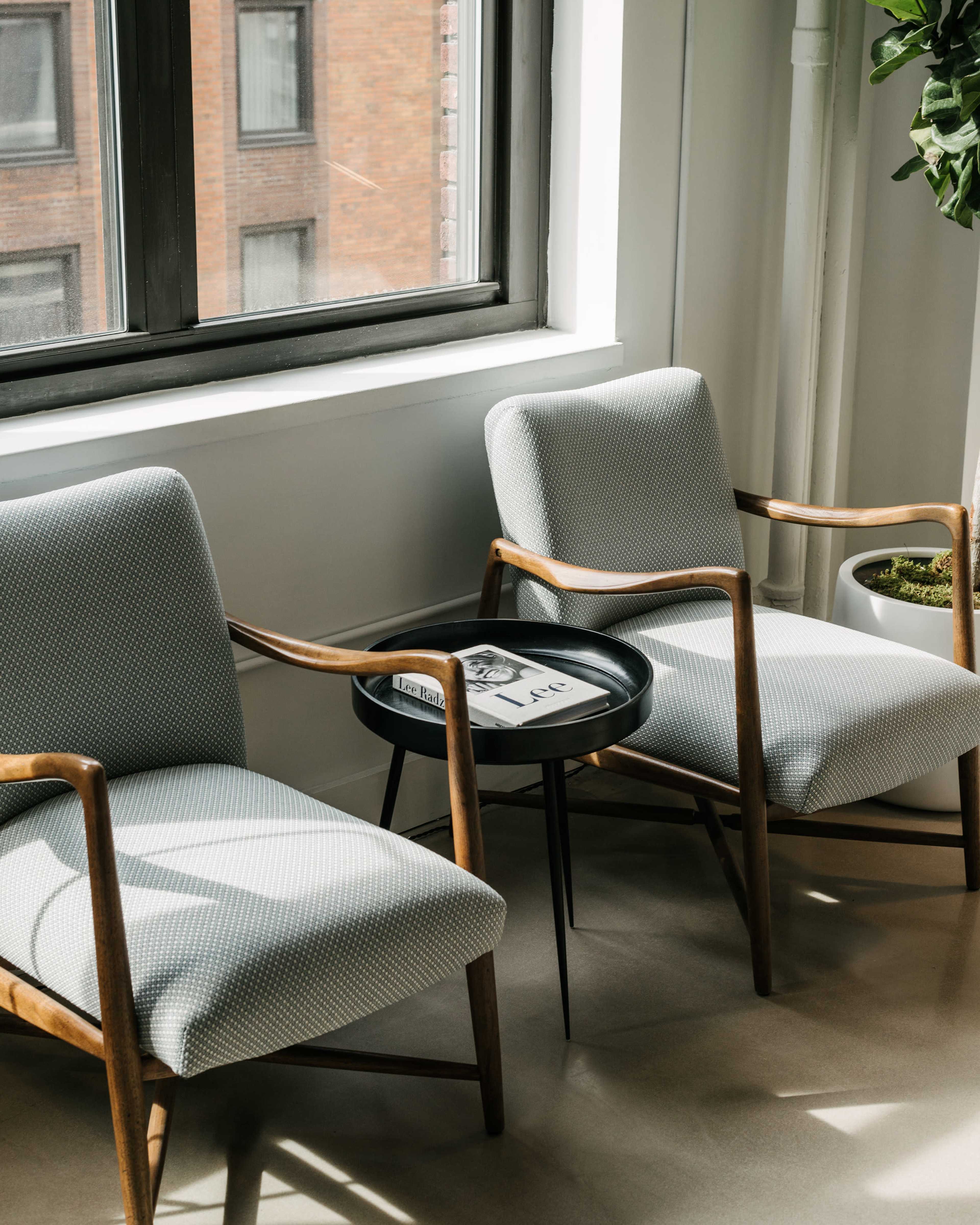 Two upholstered chairs with wooden frames are positioned beside a small black table in front of a window.