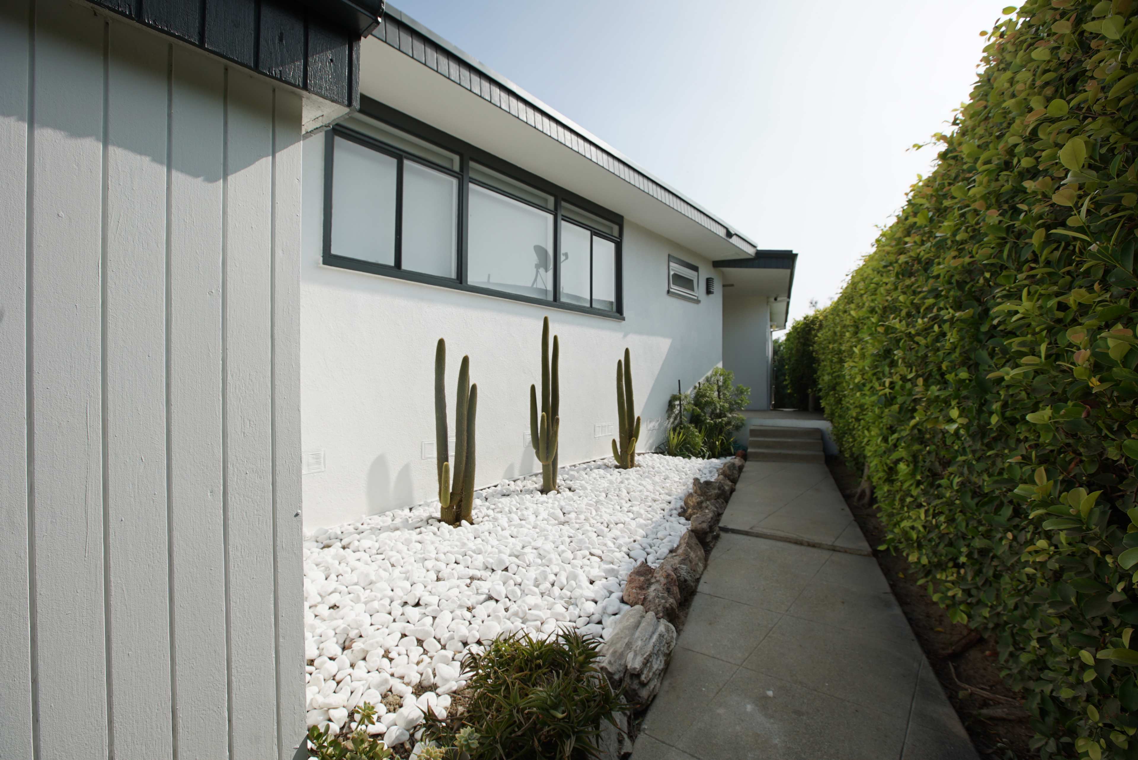 The image shows a modern house featuring a walkway alongside a garden of white stones and cacti.