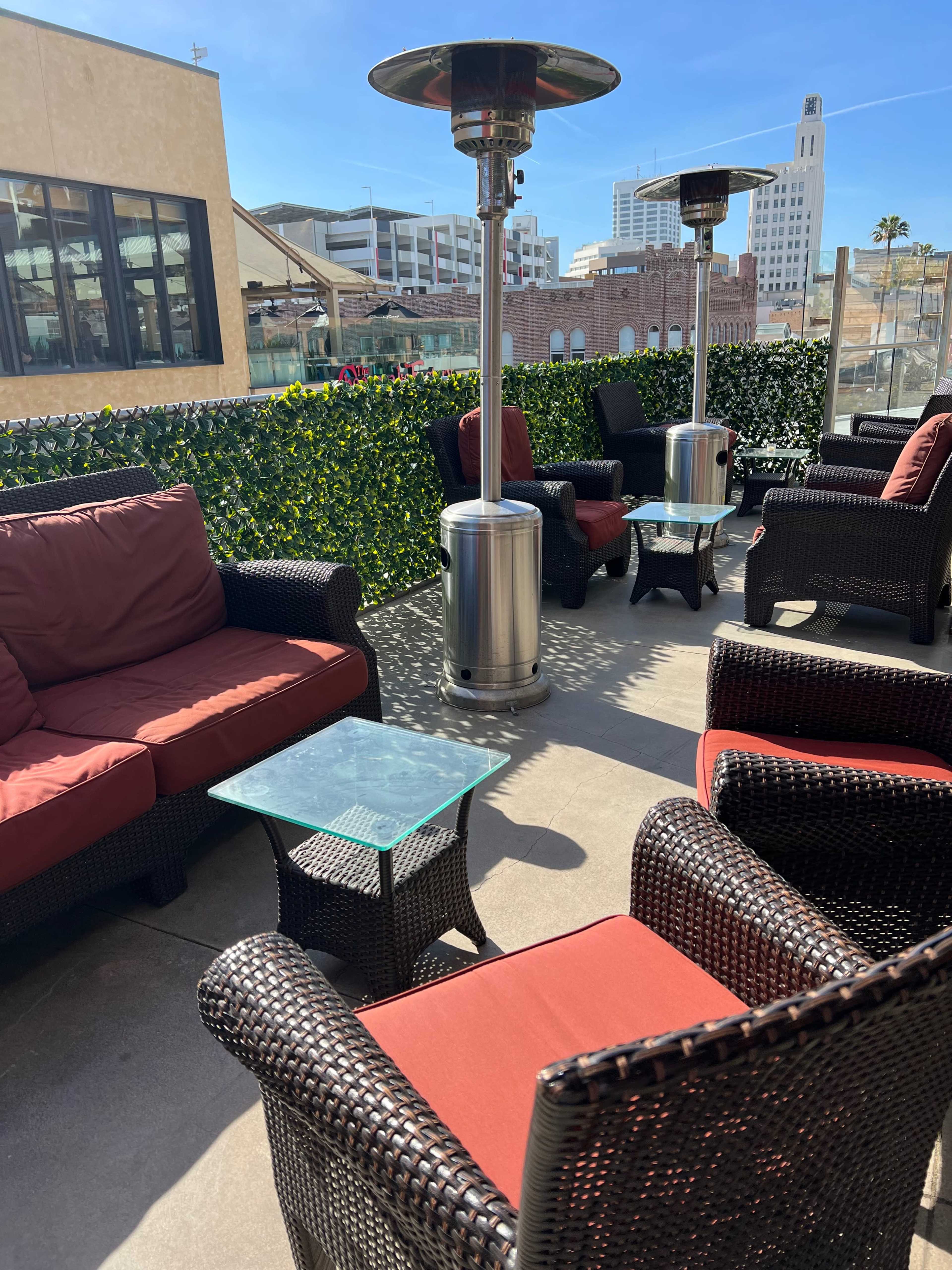A patio area with seating arrangements that include red cushion chairs, a glass-topped table, and patio heaters surrounded by greenery.