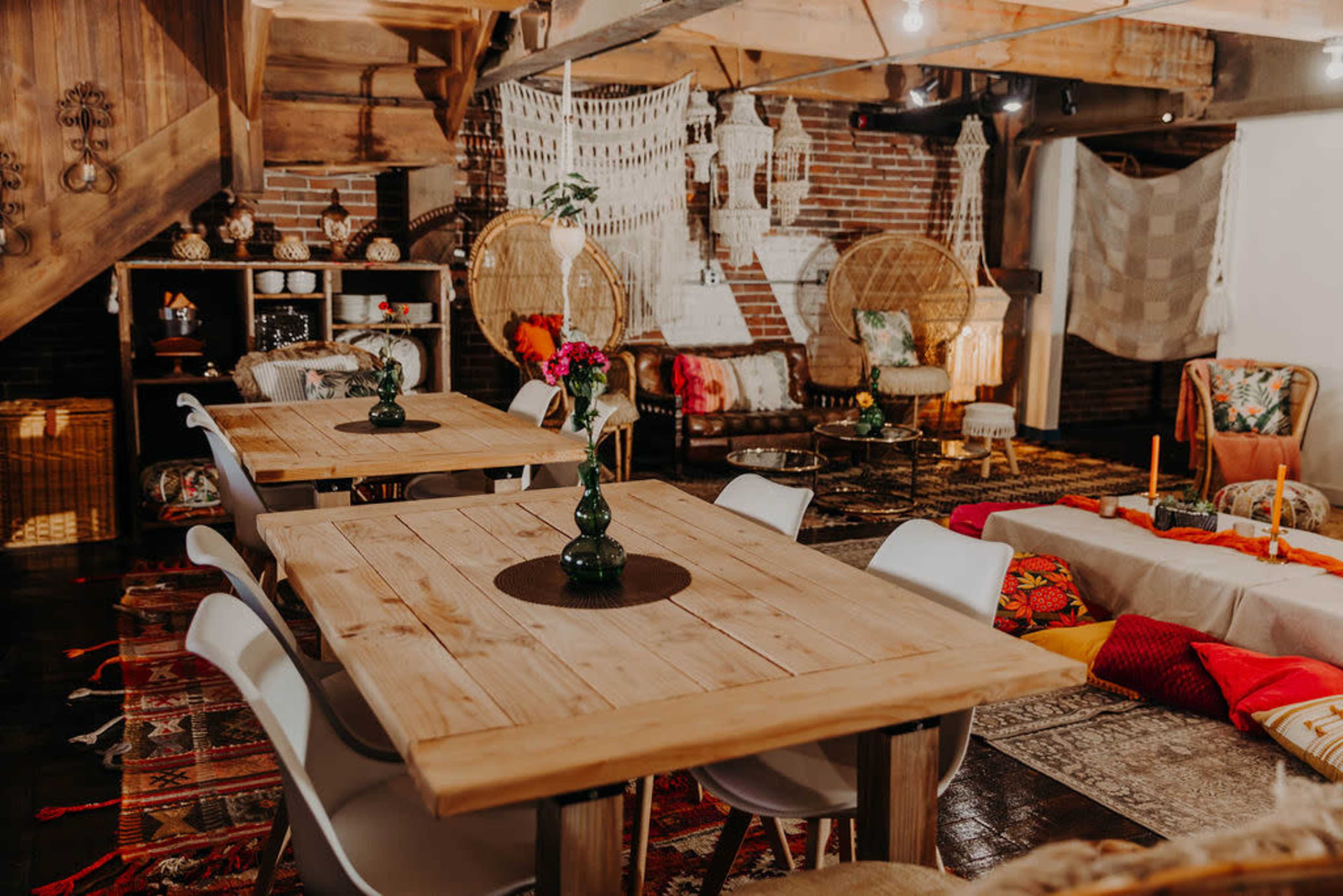 A cozy, decorated indoor space features wooden tables and various seating areas with colorful textiles and decor.