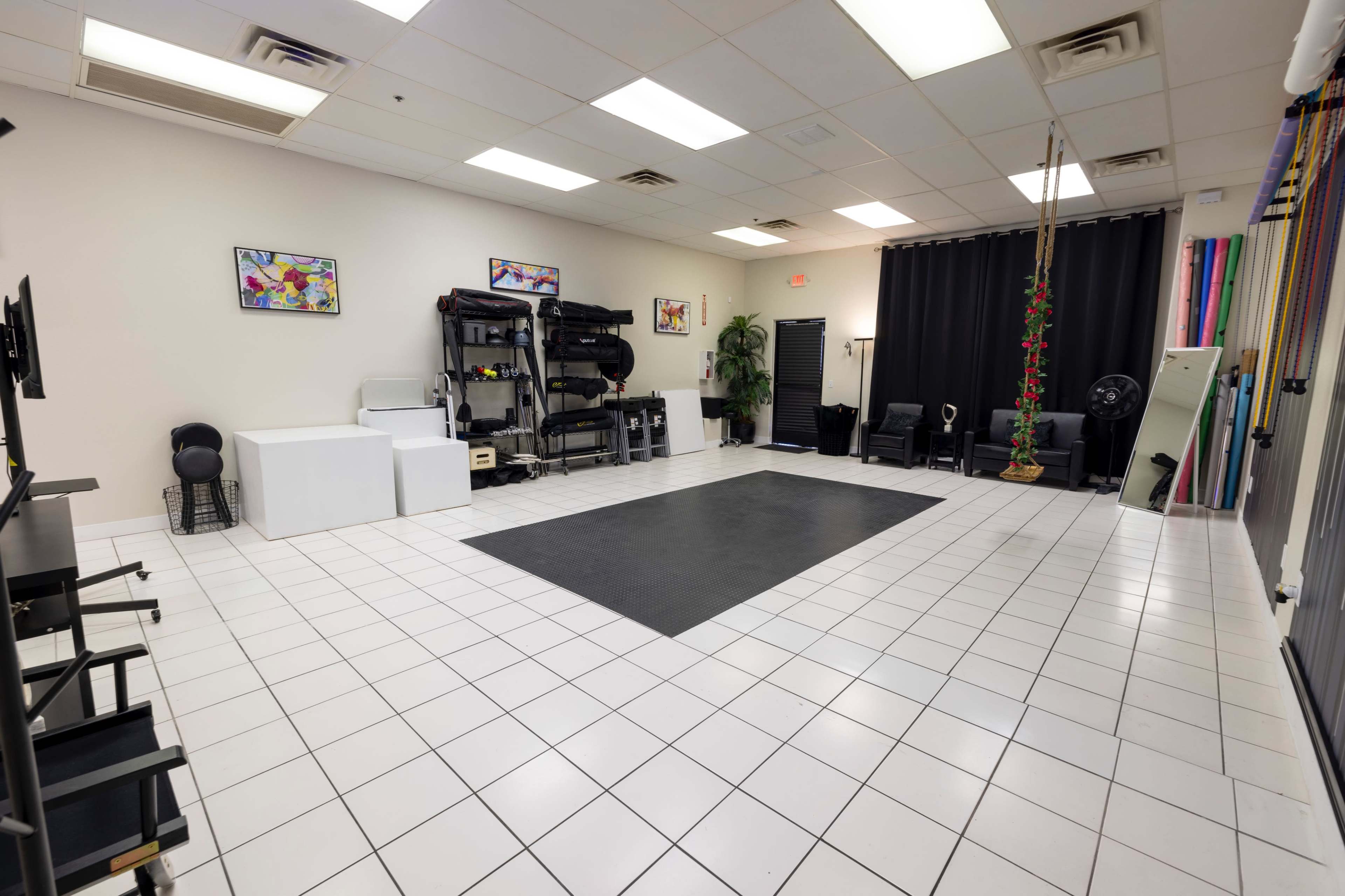 The image shows an empty studio space with tiled floors, exercise equipment against the wall, and various colorful decorations.
