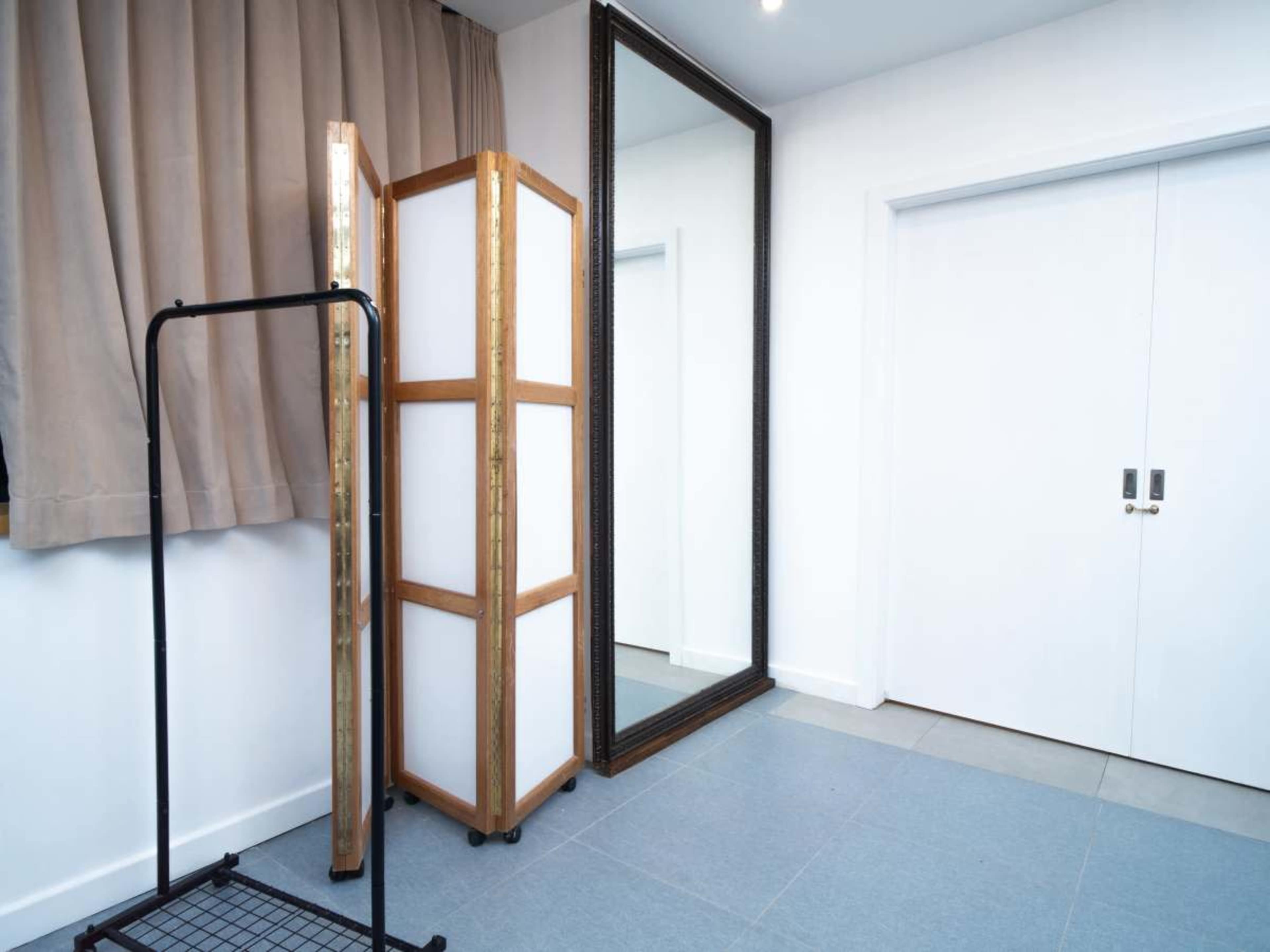 The image features a room with a large mirror, a folding screen, and a clothes rack against a wall with white double doors.