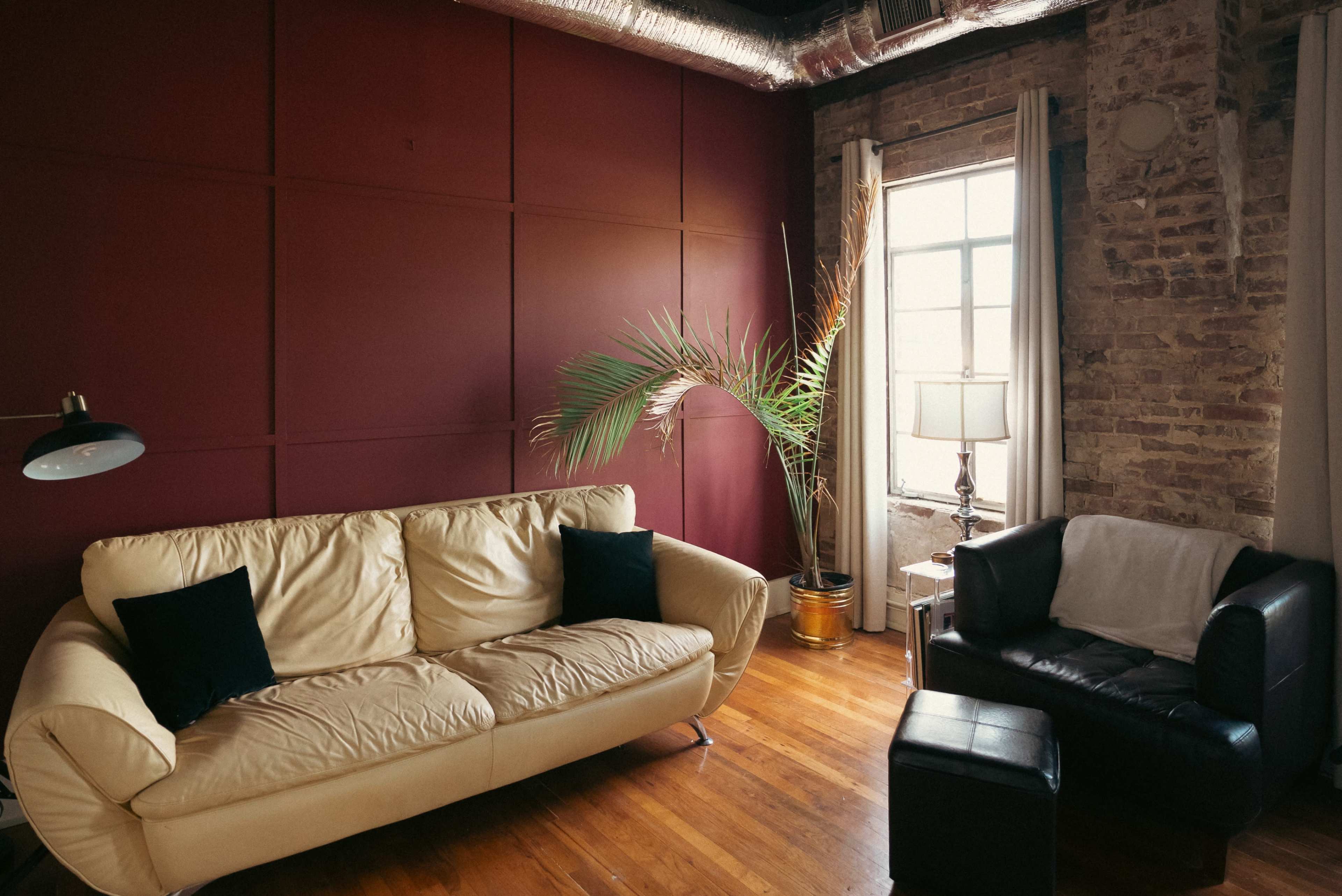 The image shows a living room with a yellow sofa, a black armchair, a tall lamp, and a potted plant beside a window.