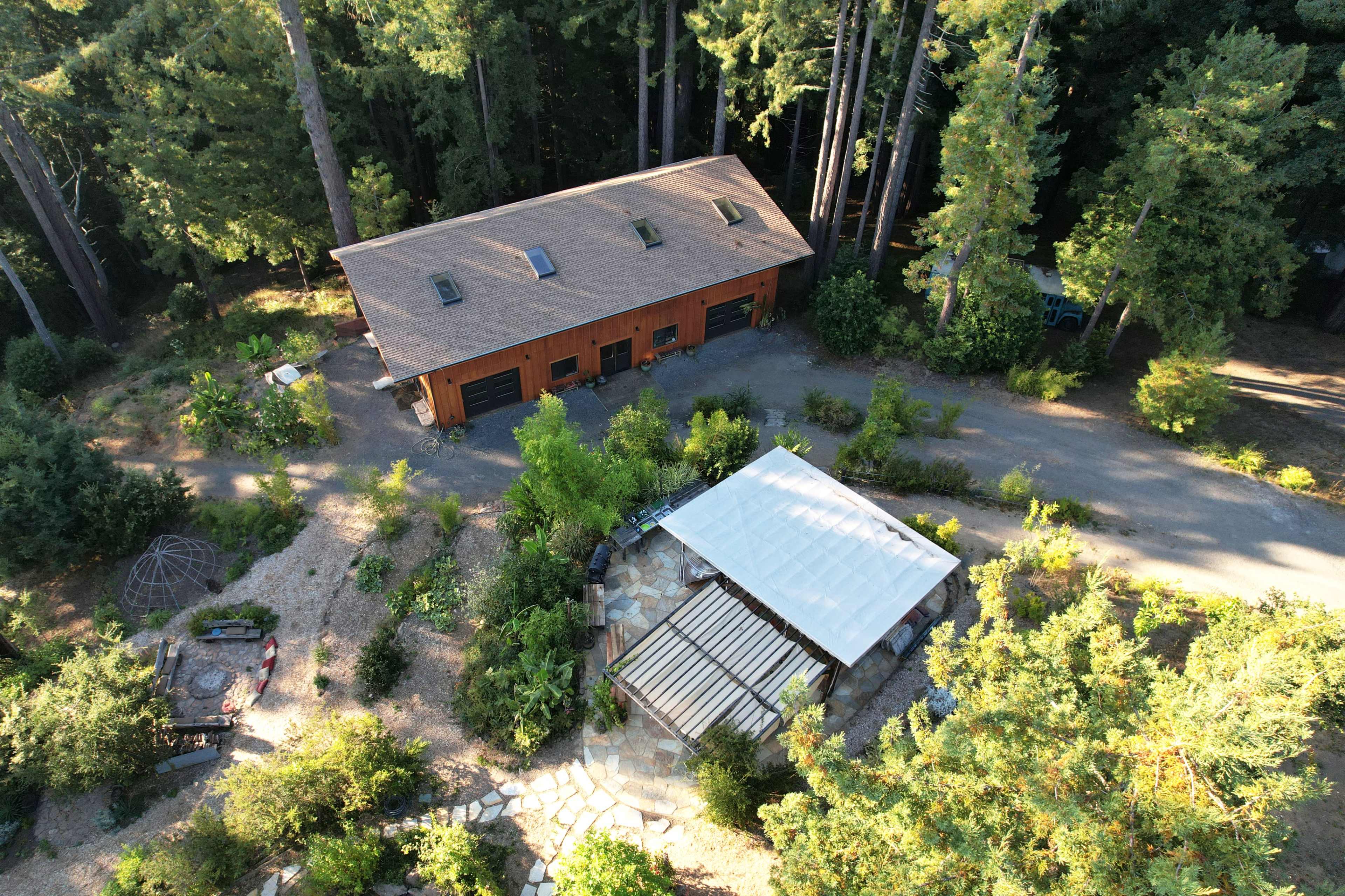 An aerial view shows a large wooden building and a covered patio surrounded by greenery and trees.