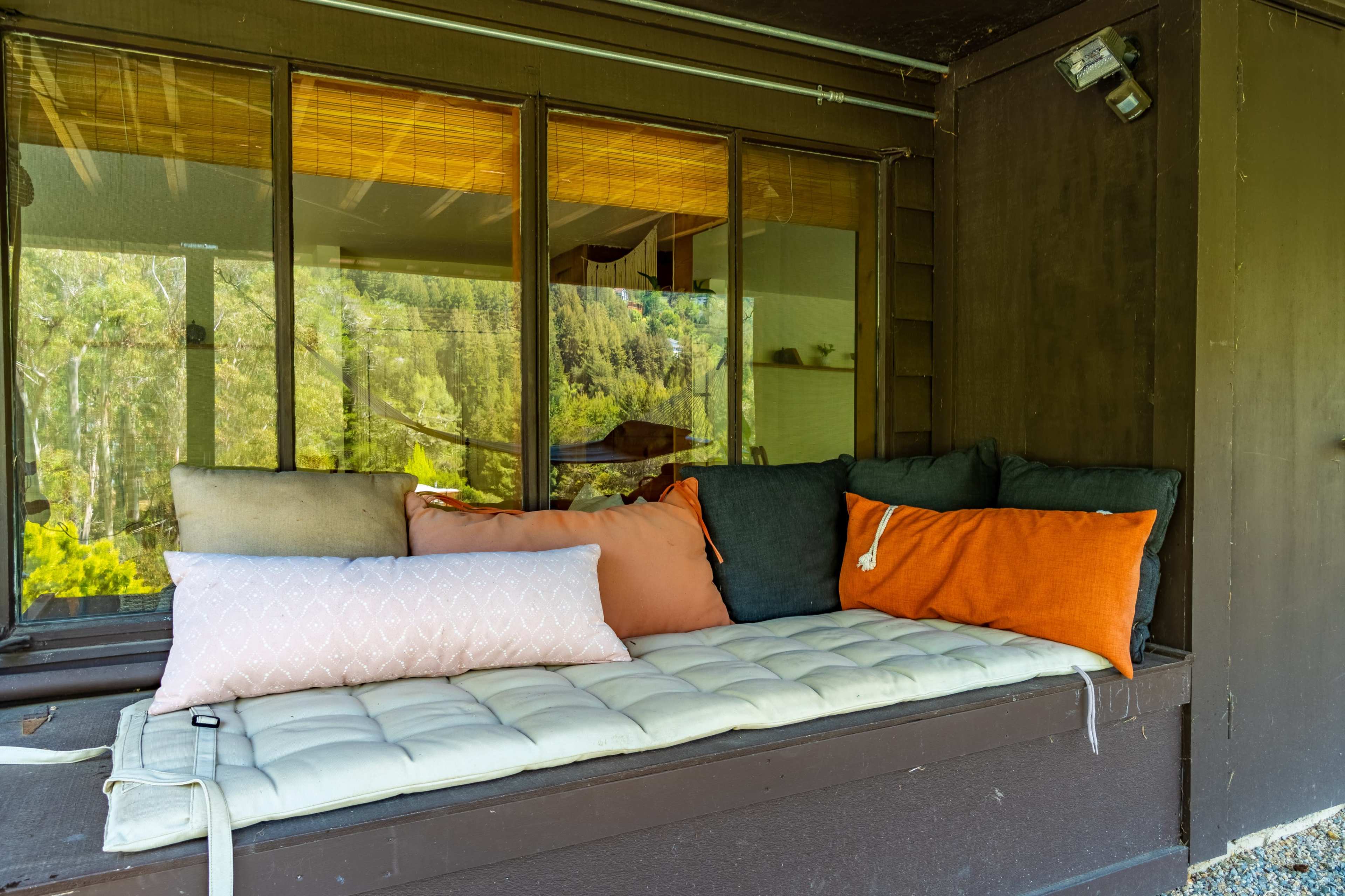 A cozy seating area with cushions arranged on a wooden platform near large windows overlooking a forested landscape.