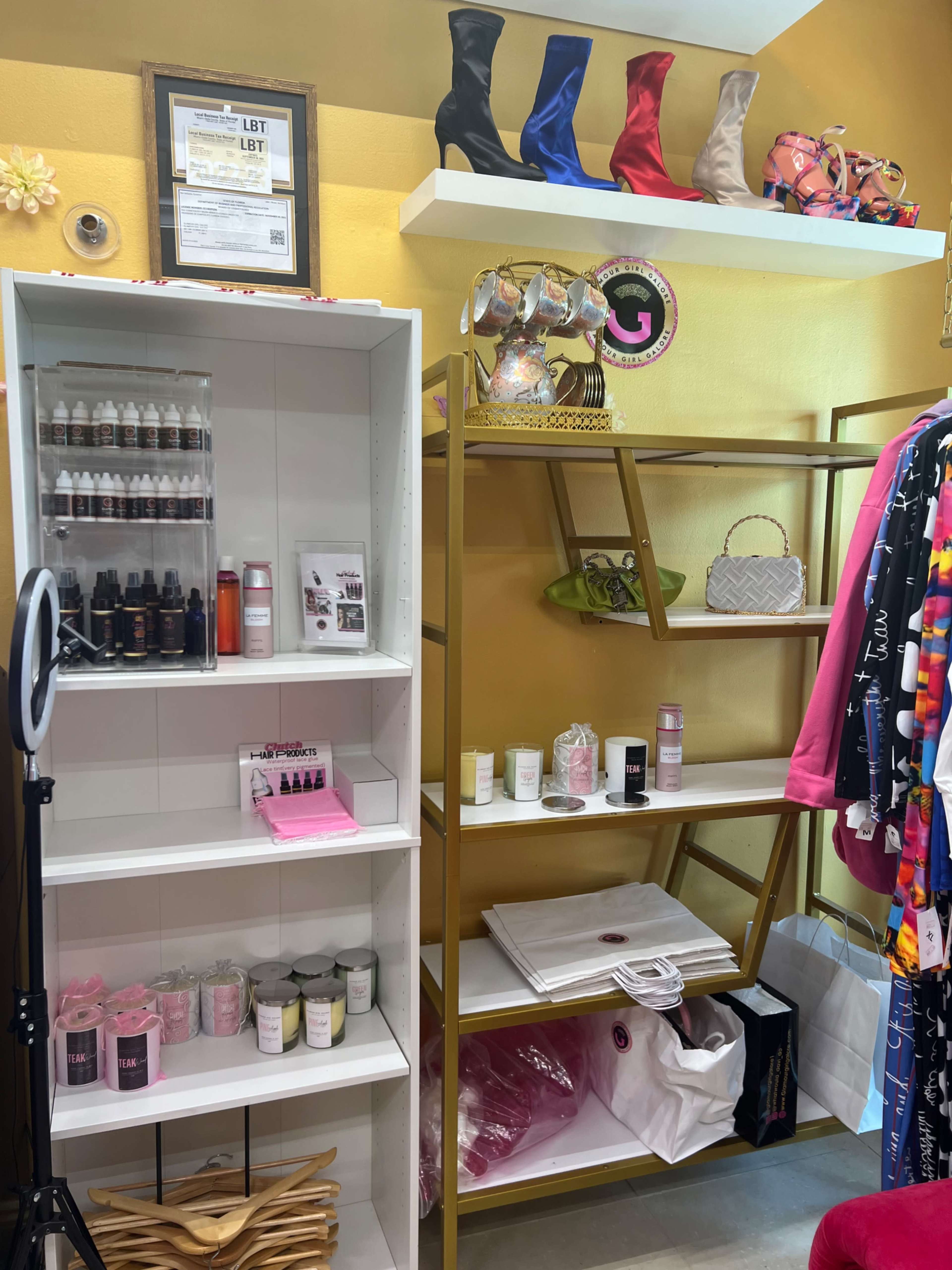 The image shows a small retail space featuring shelves stocked with beauty products, clothing items, and high-heeled boots arranged on a display.