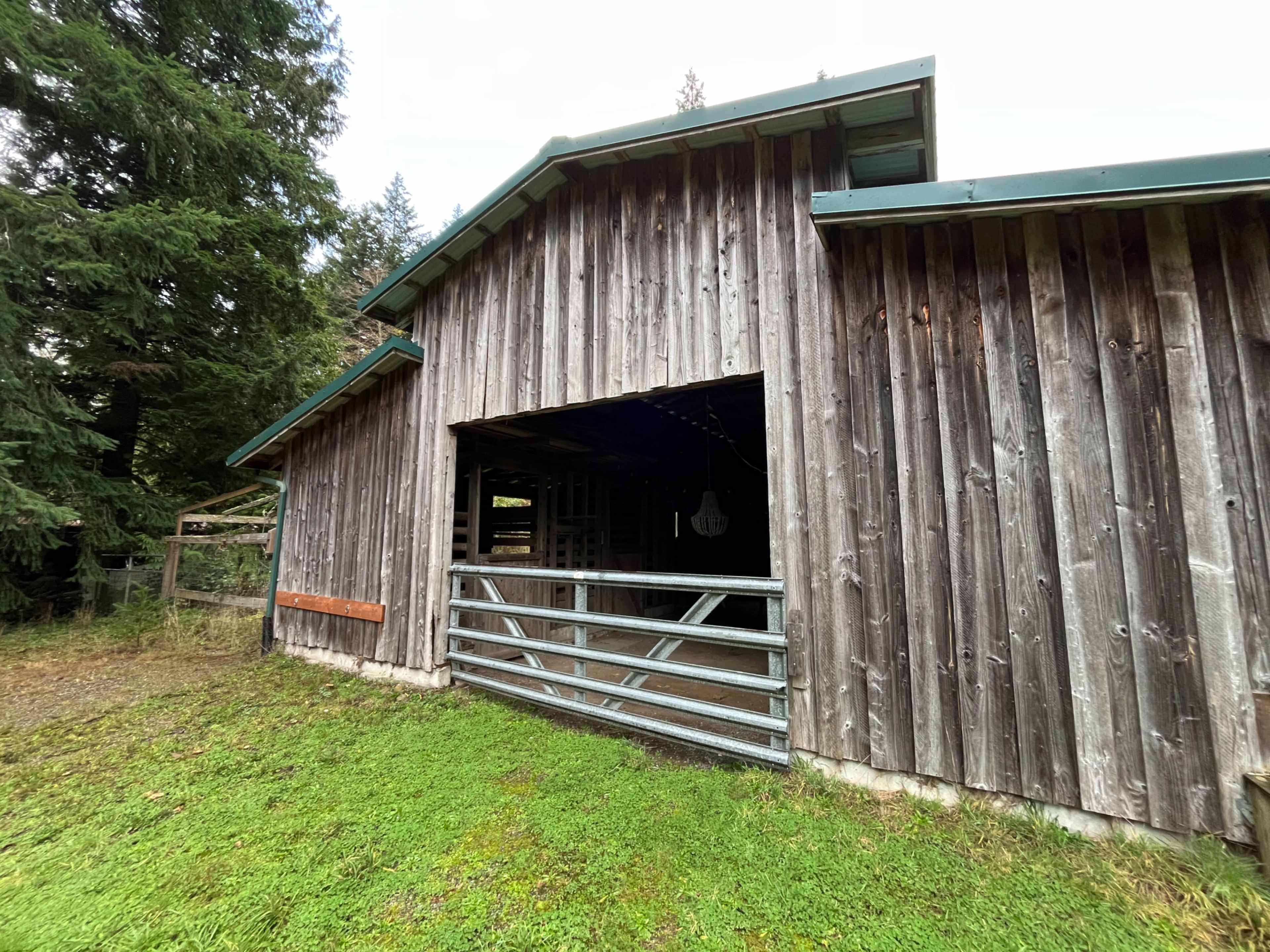 The image shows a rustic wooden barn with an open front and a grassy area surrounding it.