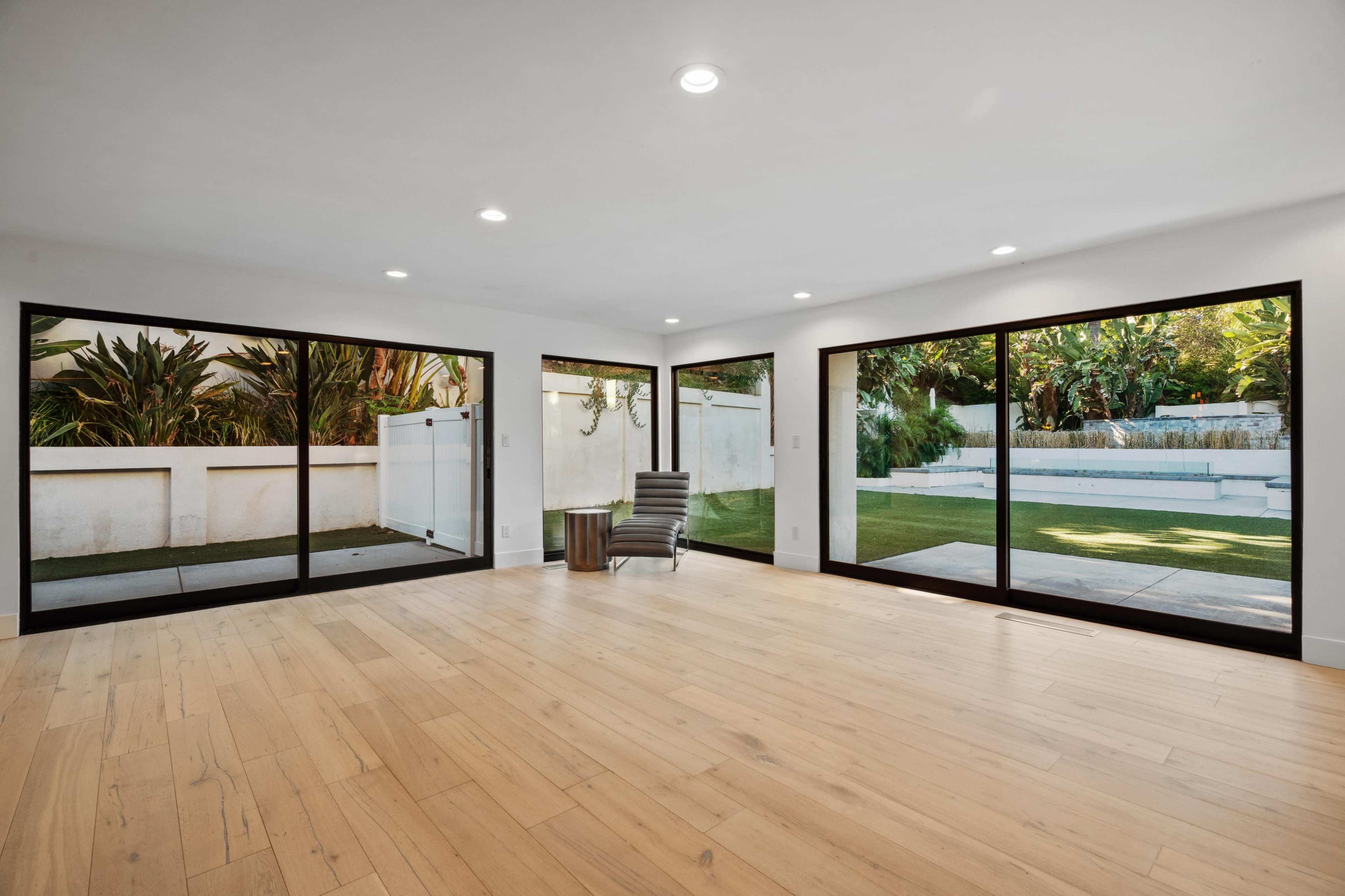 A spacious room with large glass sliding doors overlooks a landscaped outdoor area featuring greenery and a small water feature.