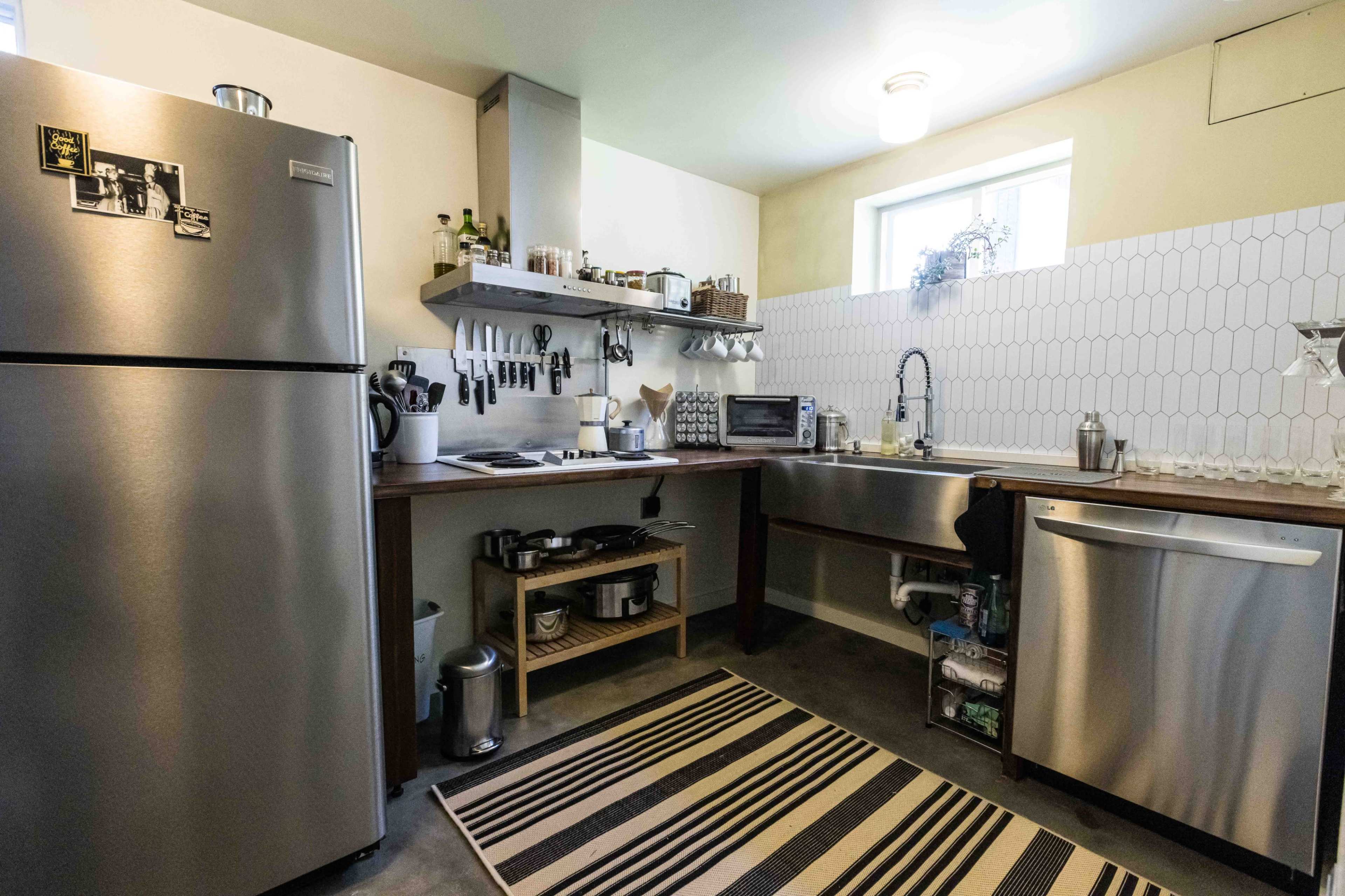 The image shows a modern kitchen featuring stainless steel appliances, a wooden countertop, and a striped area rug.