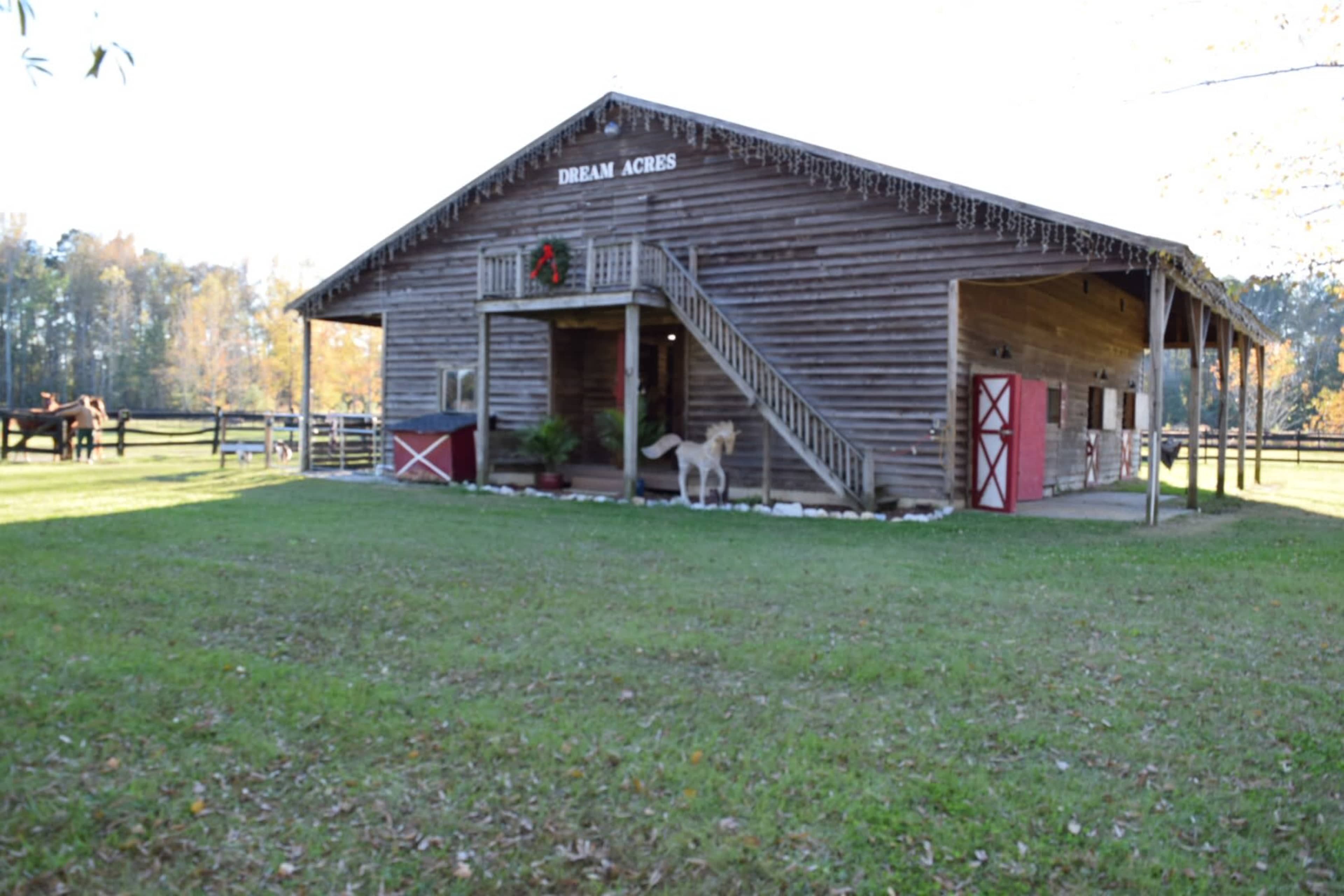 A wooden barn labeled "Dream Acres" stands next to a grassy area, featuring stairs and red doors.