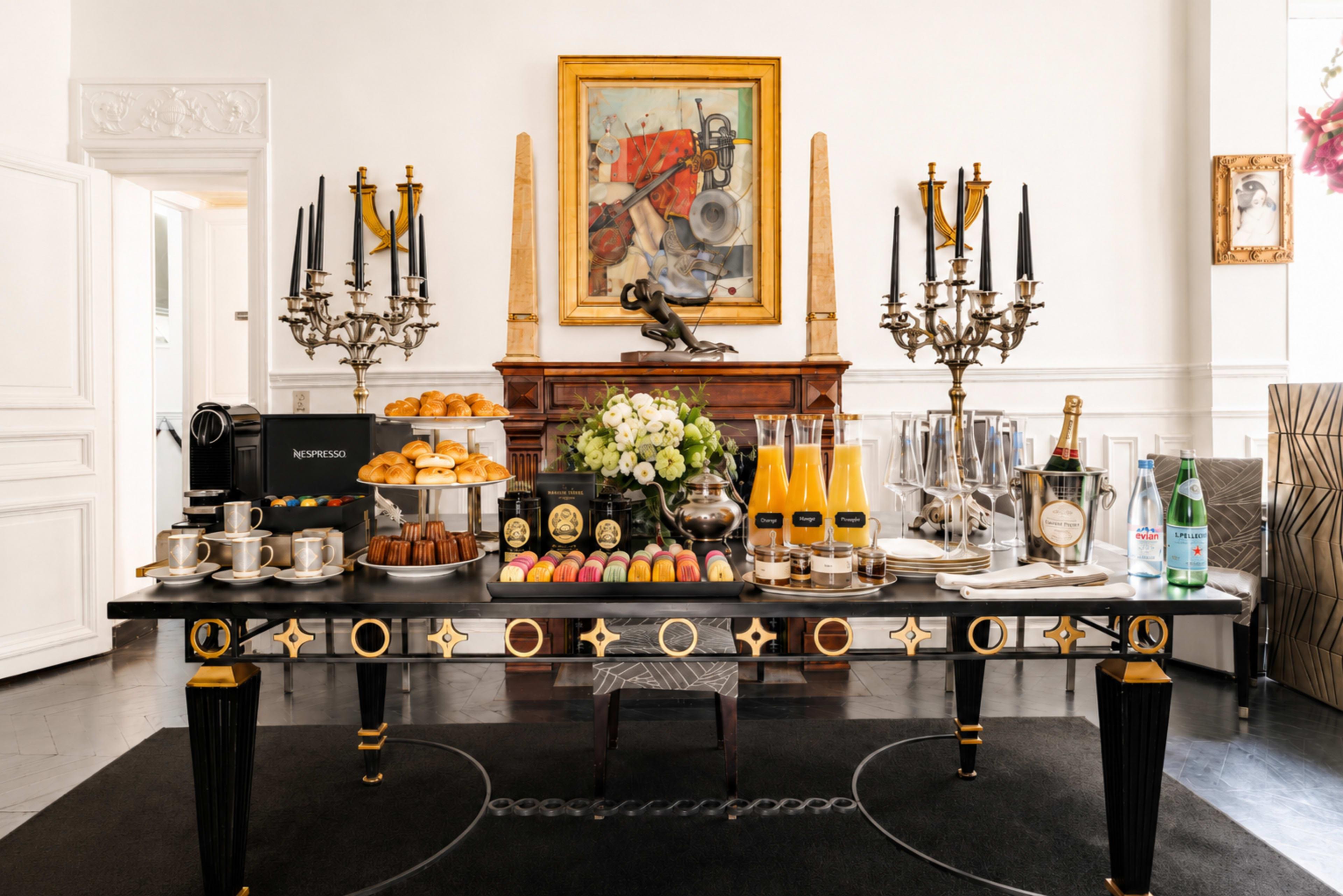 A lavish buffet table is set with various pastries, drinks, and decorative items in an elegantly styled room.