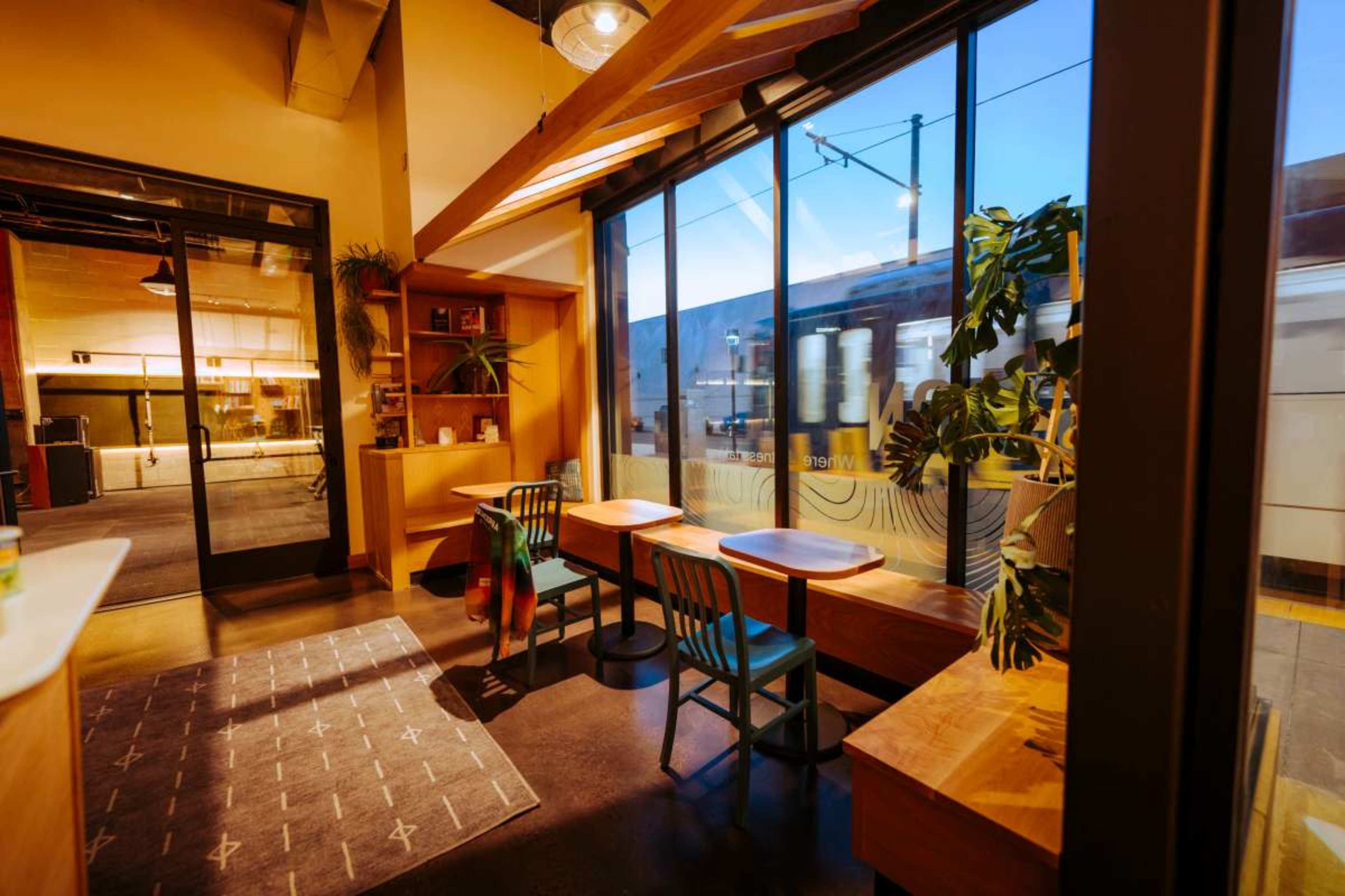 The image shows a modern café interior with wooden furniture, large windows, and a view of a train passing outside.
