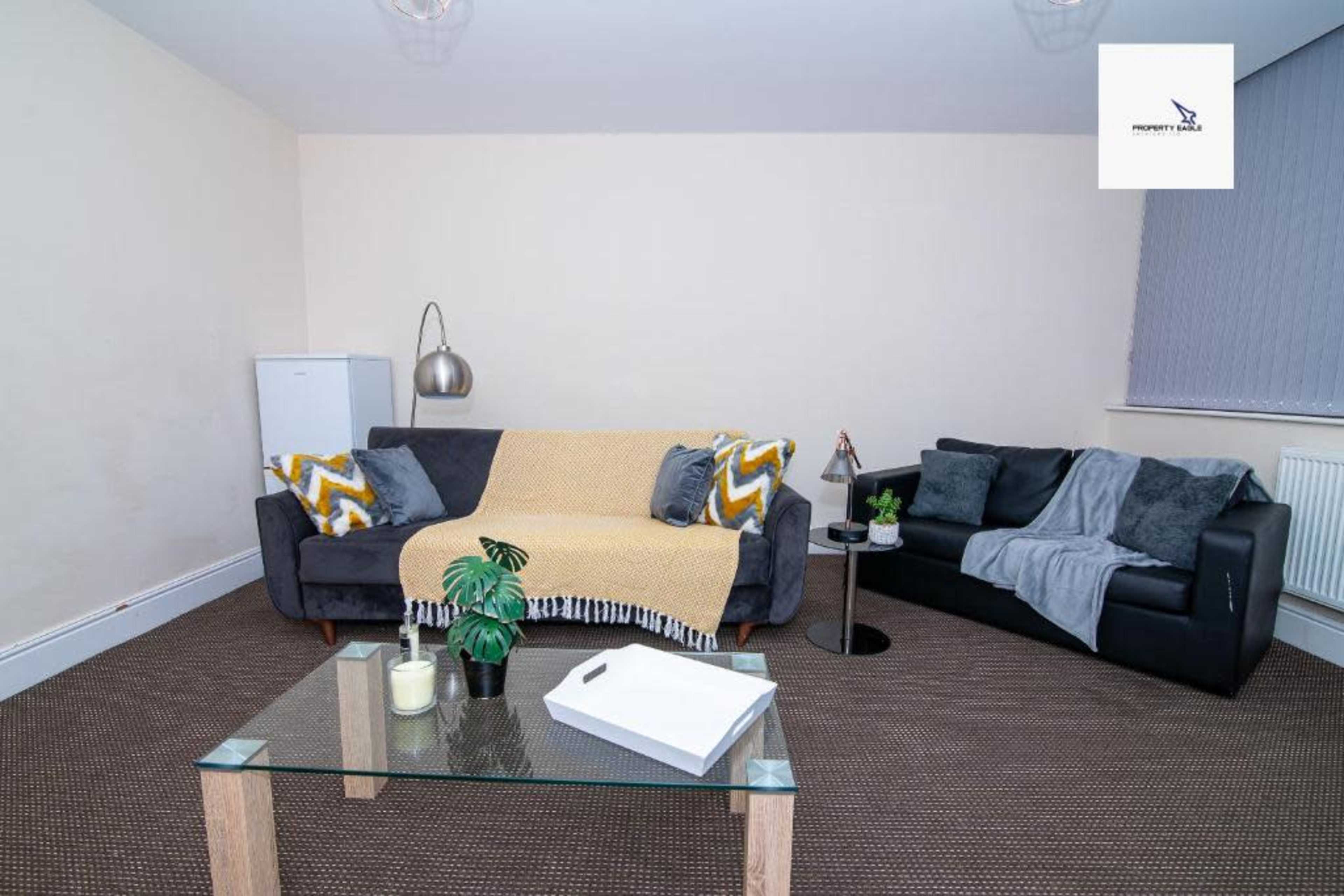 A living room features two sofas with decorative throws, a glass coffee table, and a small plant, with minimal decor.