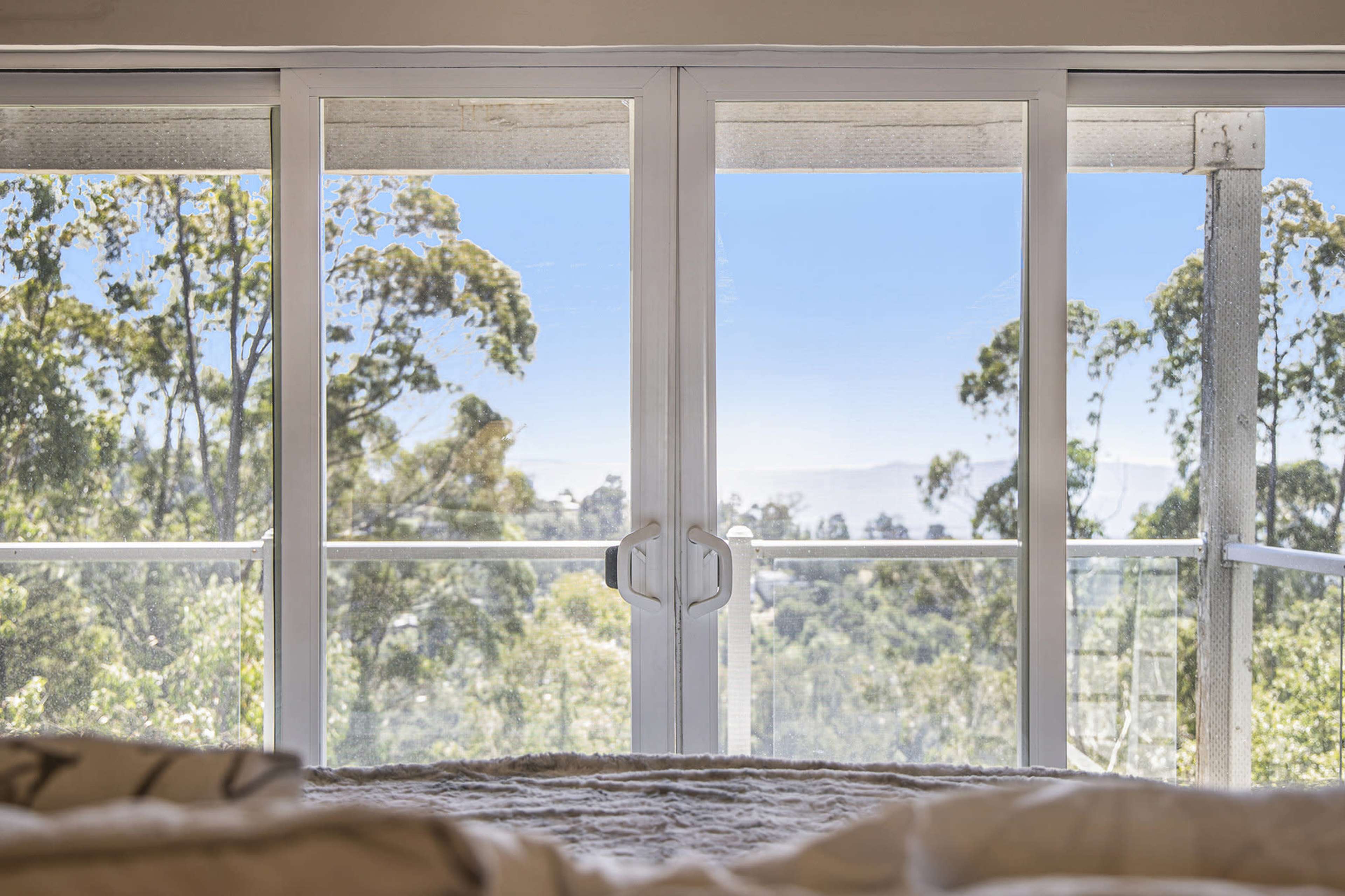 A bedroom with large glass sliding doors providing a view of trees and mountains in the distance.