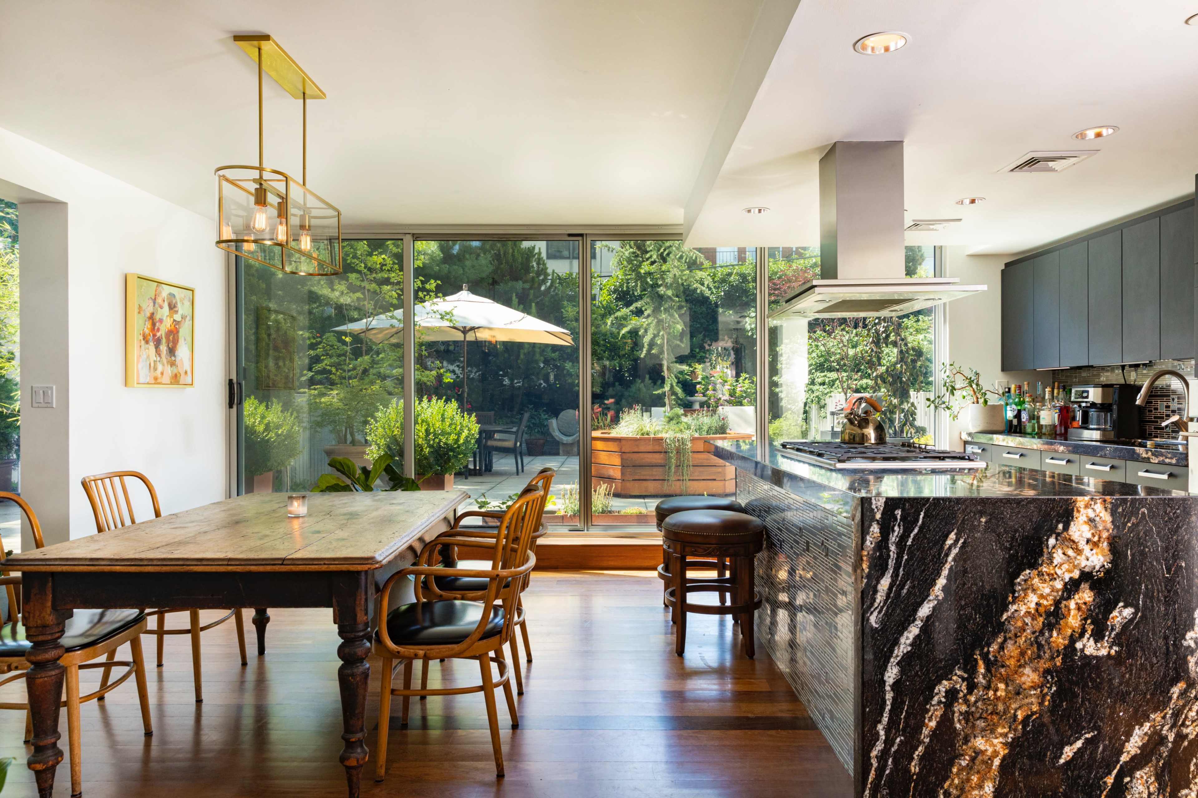A modern kitchen with a dining table and a view of a patio featuring greenery and an outdoor umbrella.