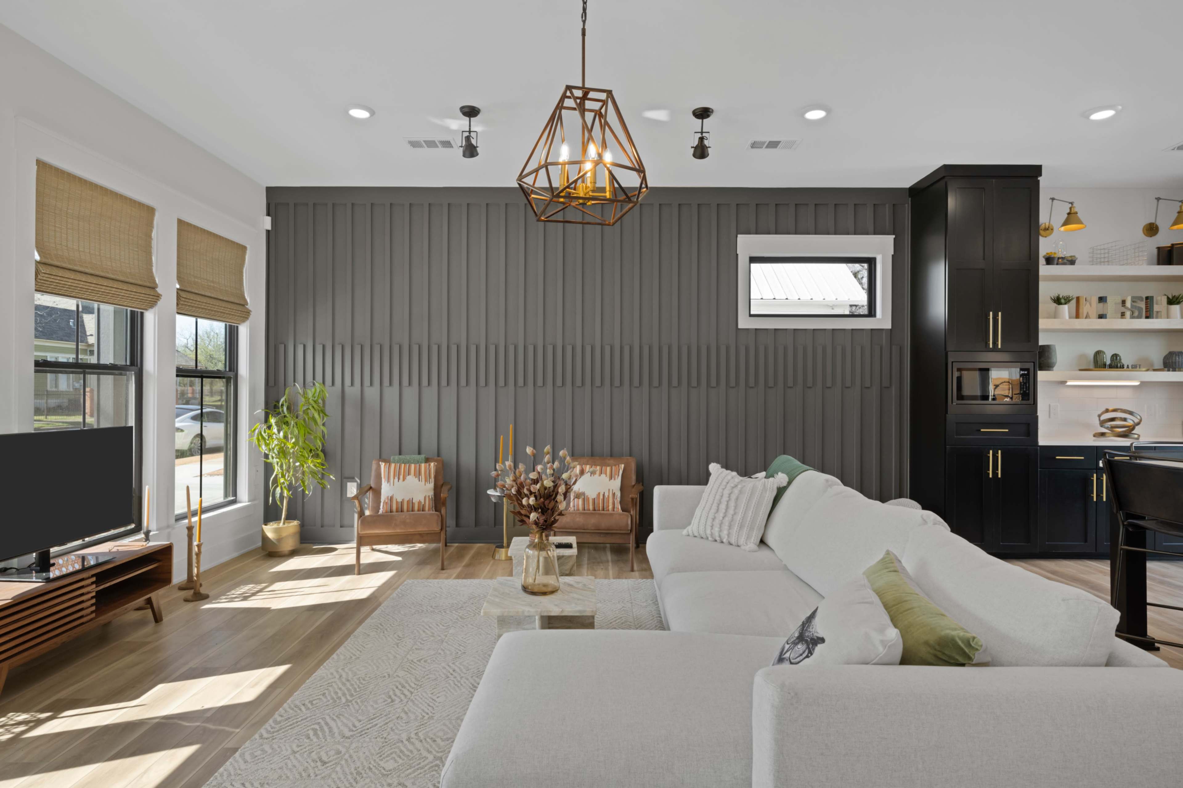 A modern living room with a gray feature wall, a white sectional sofa, and a kitchen area in the background.