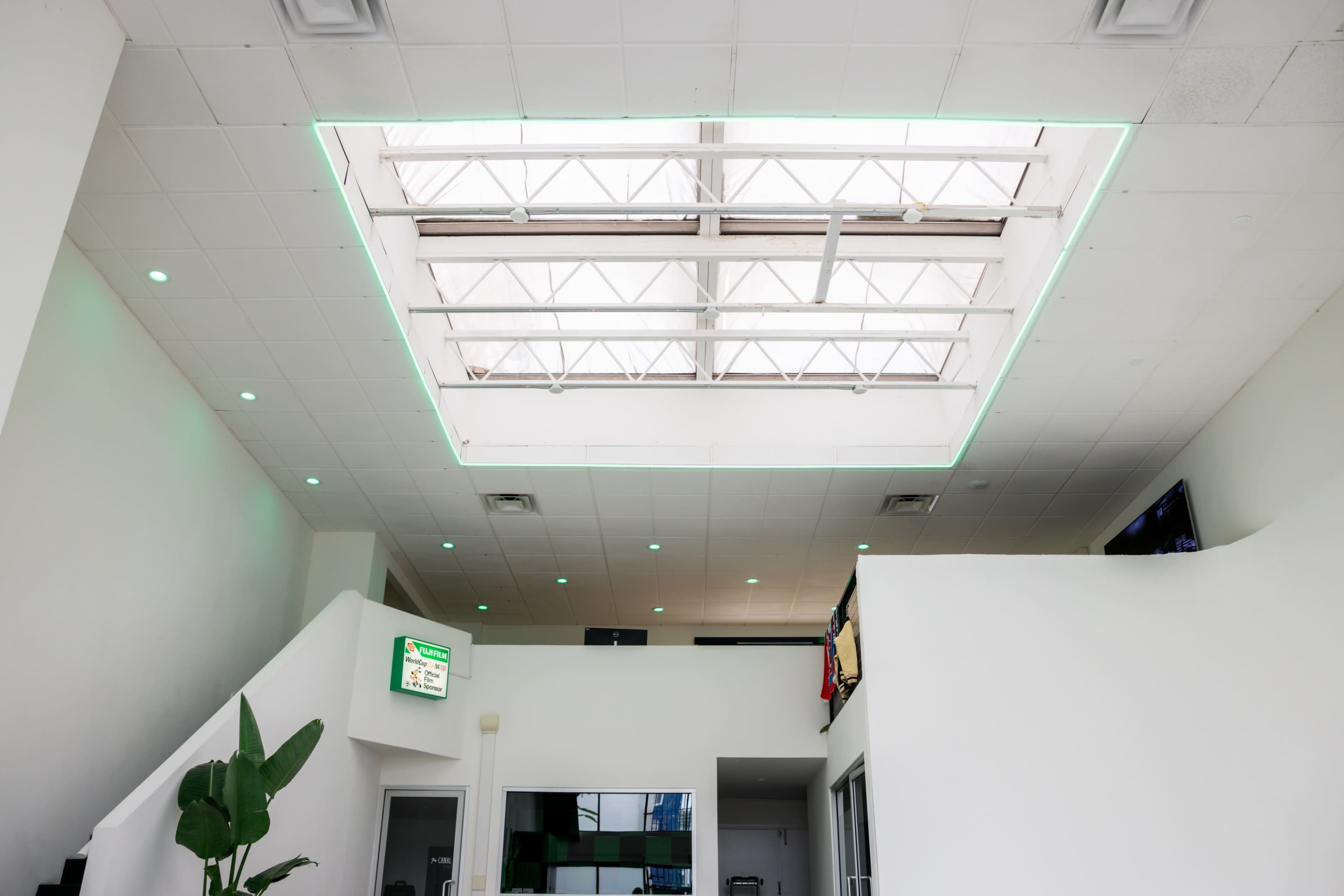 A modern interior space with a skylight framed by a rectangular green light, surrounded by white walls and a staircase.
