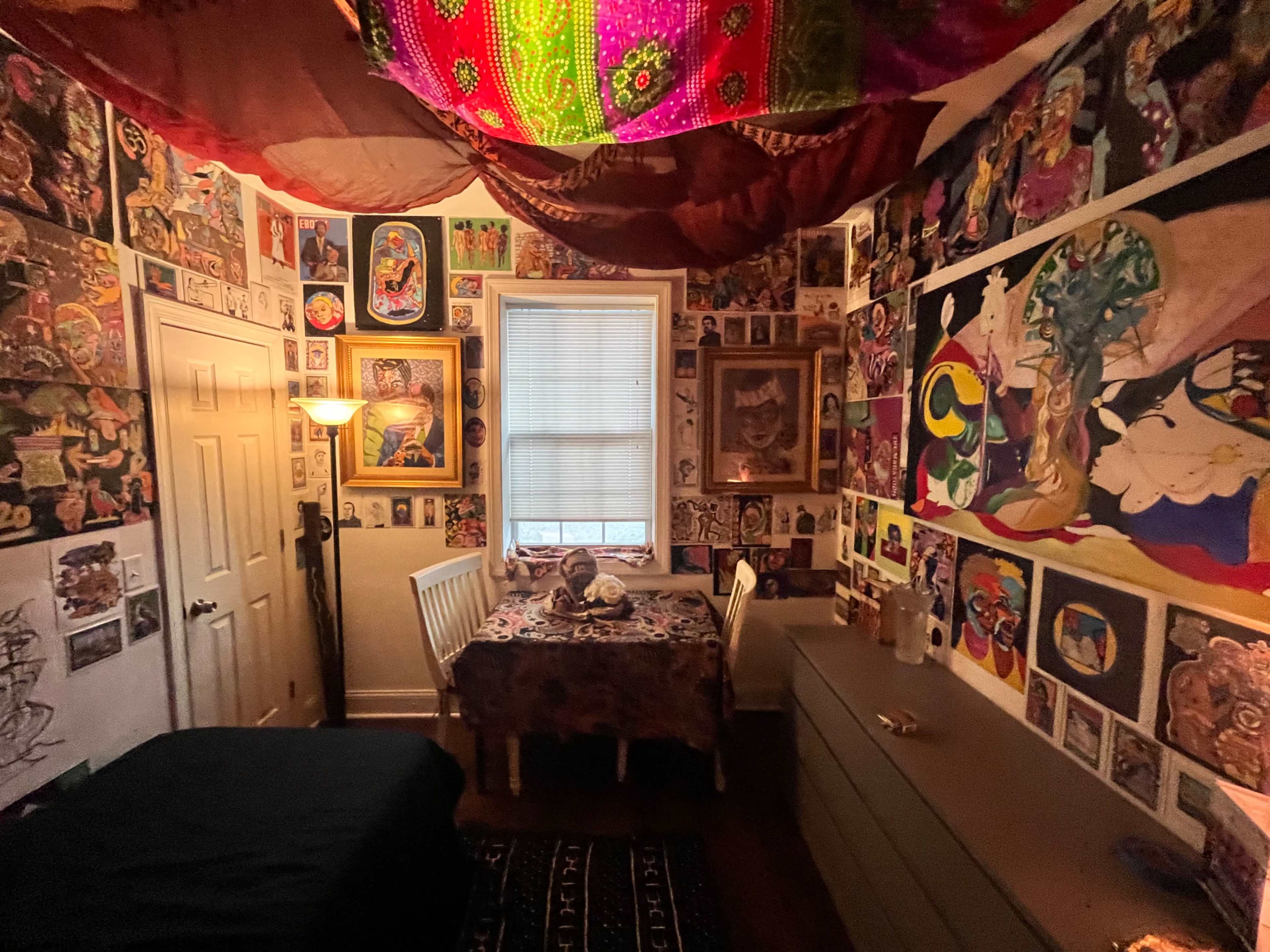 A small, colorful room features walls adorned with various artworks and decorations, with a table and chairs in the center.