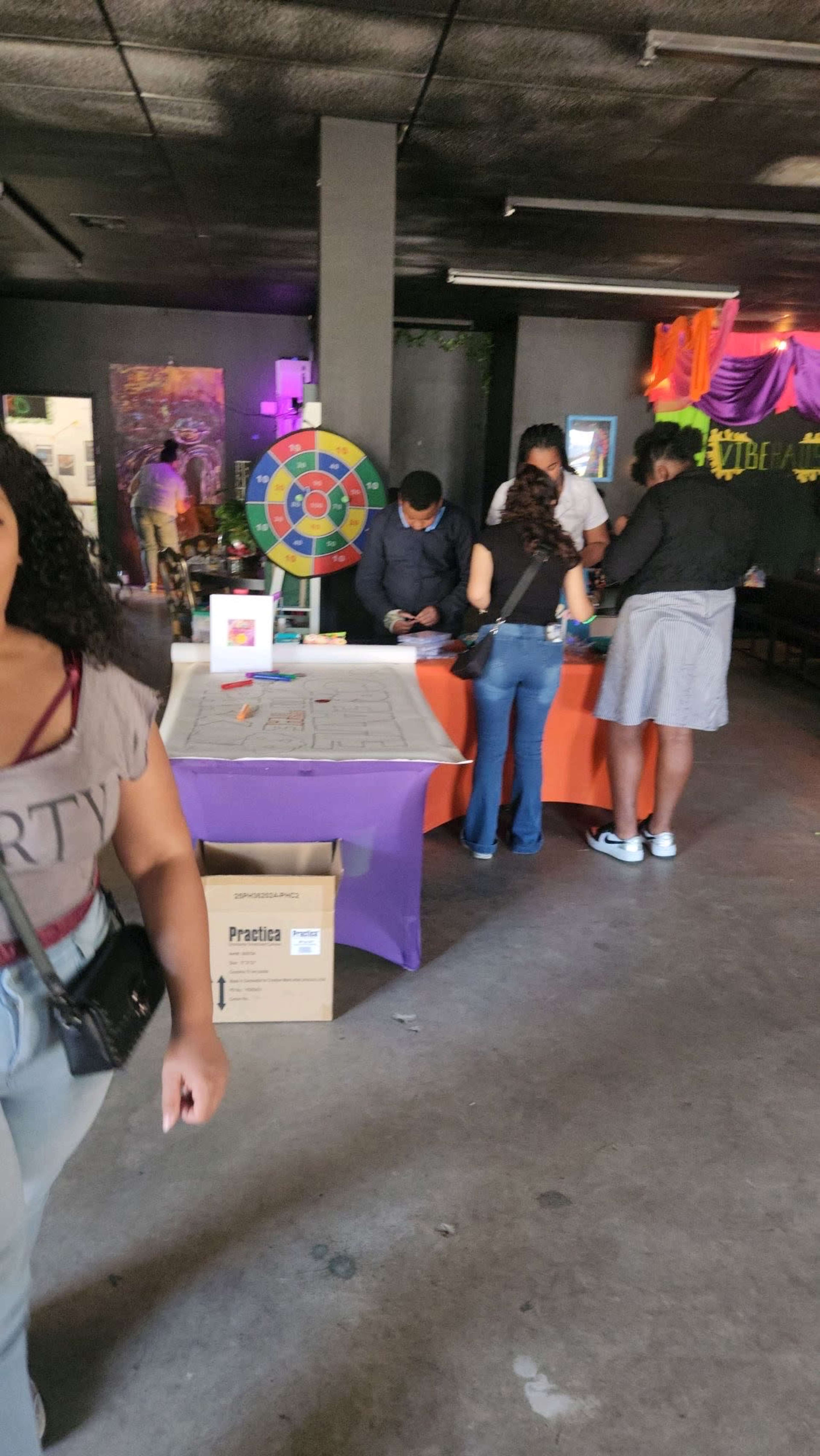 A group of people is gathered around a table with a game wheel in a decorated indoor space.