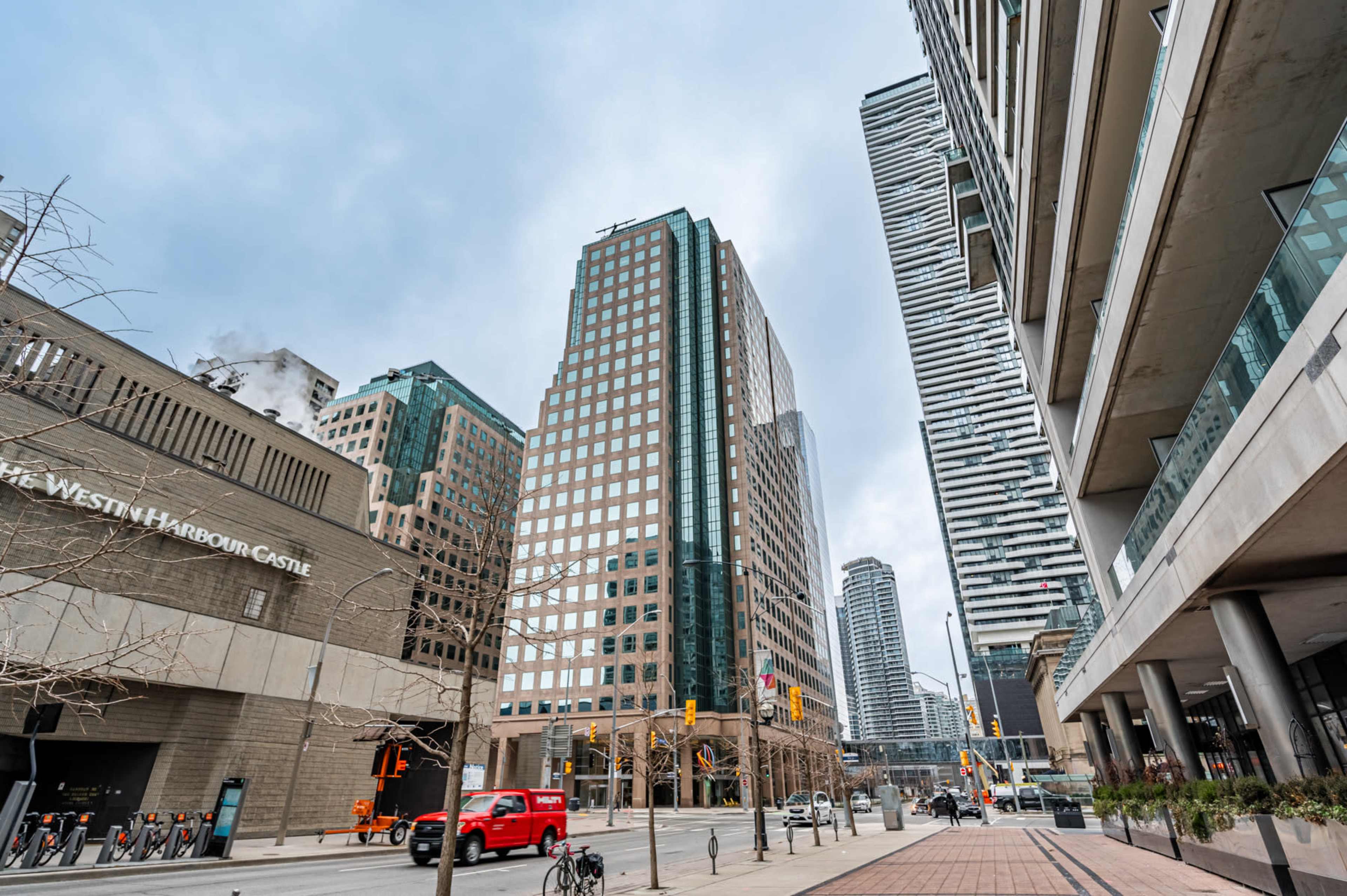 A street scene in a city with modern skyscrapers, including the Westin Harbour Castle hotel, and a red truck parked along the curb.