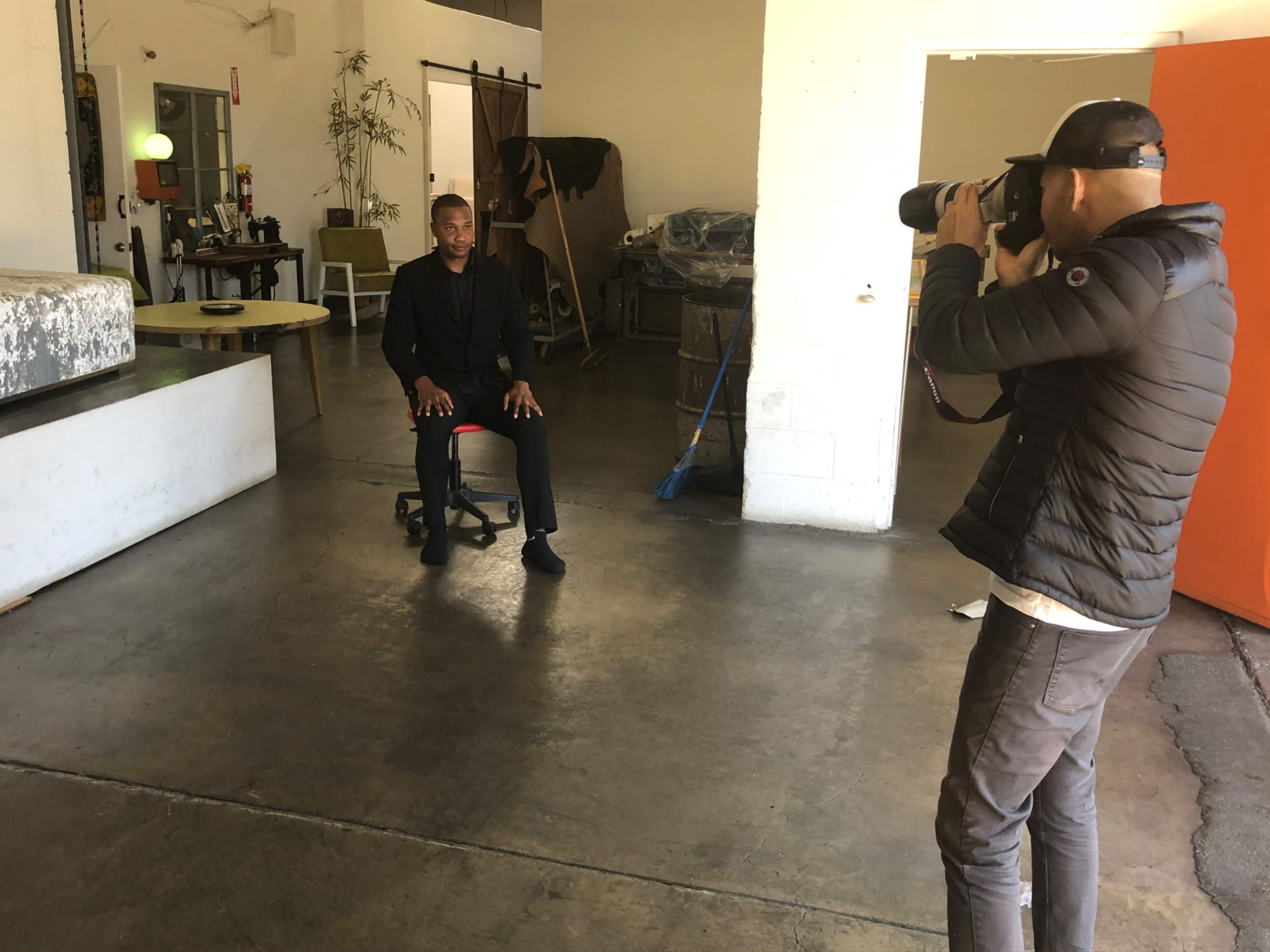 A photographer captures a seated subject in a spacious studio featuring various props and furniture.