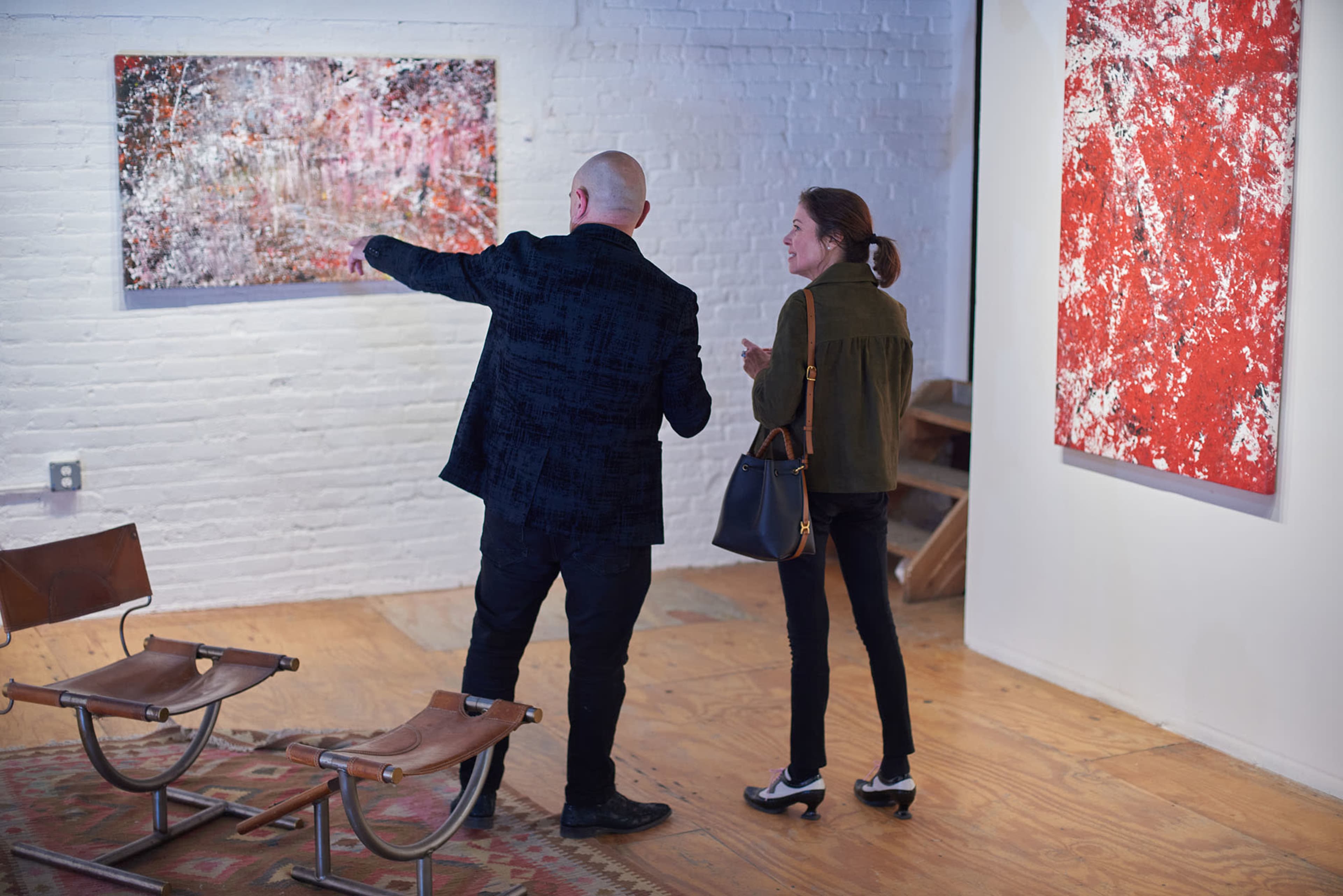 Two individuals are engaging in conversation while looking at abstract art on the walls of a gallery.