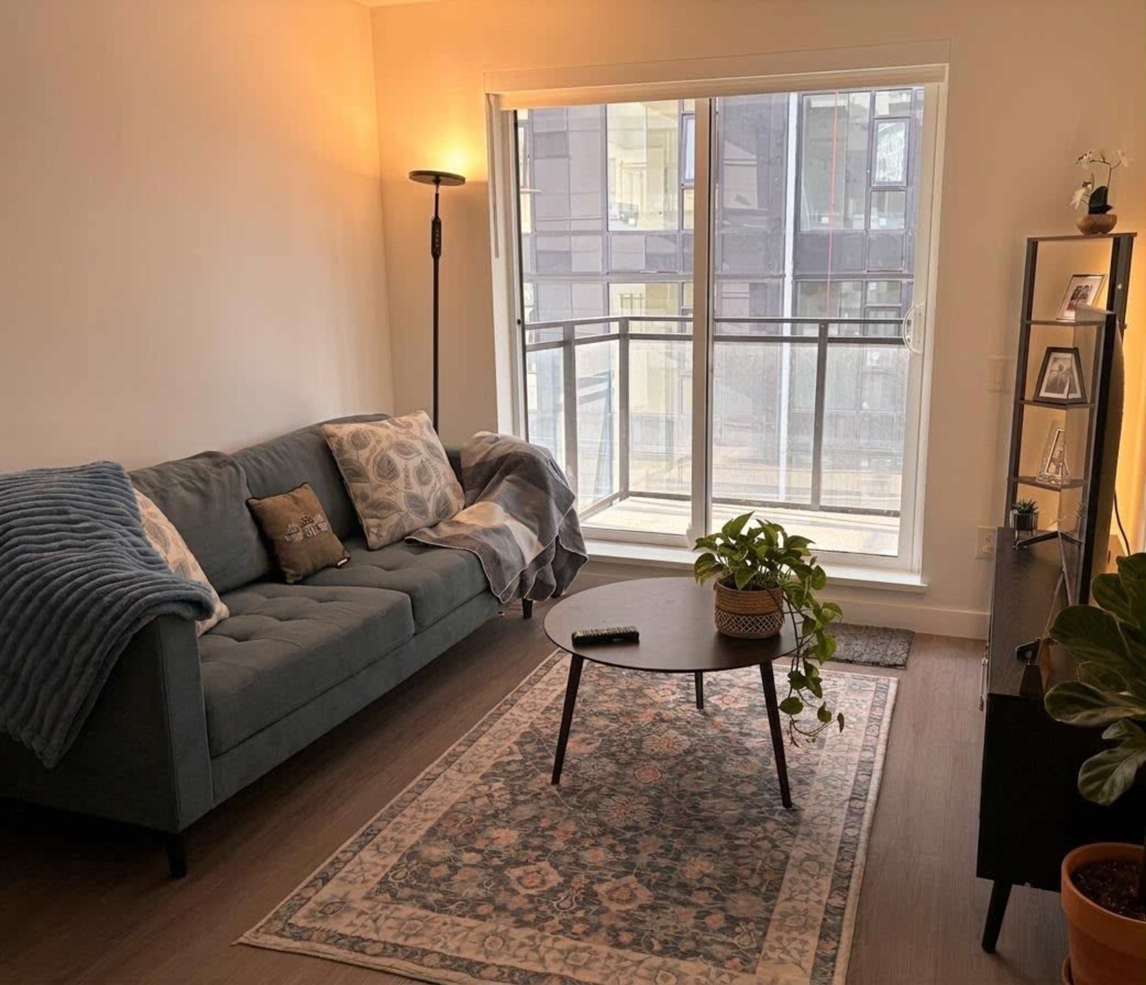The image shows a modern living room with a teal sofa, a round coffee table, and large windows providing natural light.