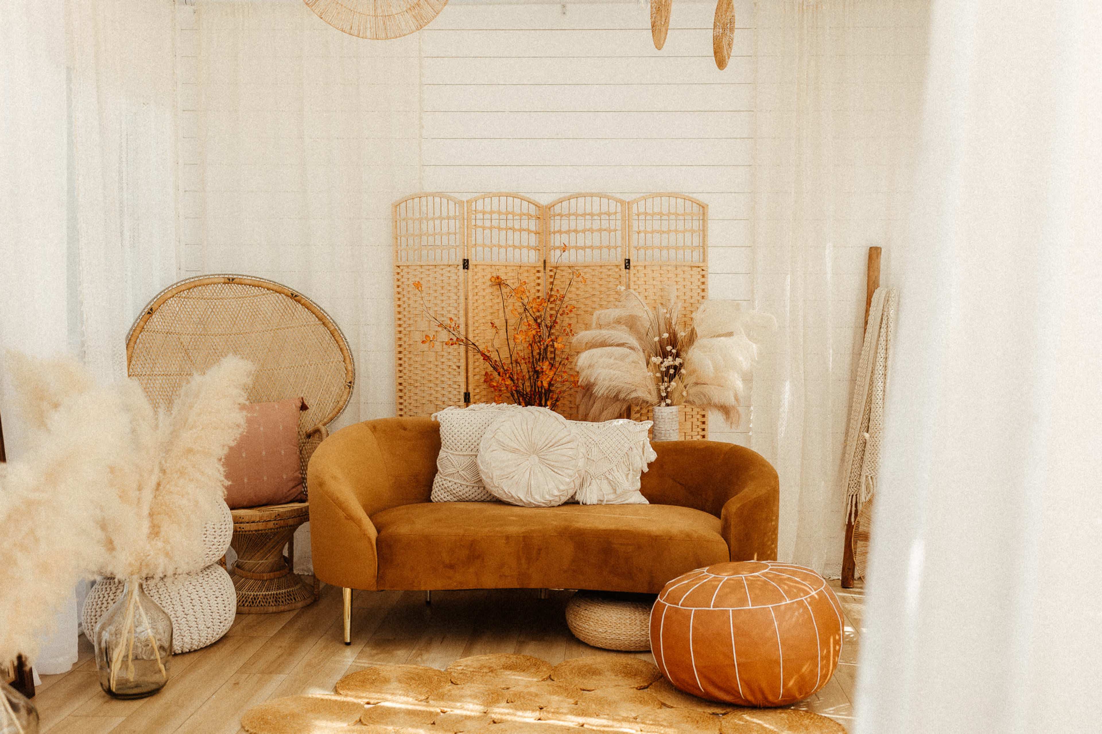 The image shows a cozy living space with a mustard-colored couch, decorative pillows, a woven screen, and various textured decor elements.